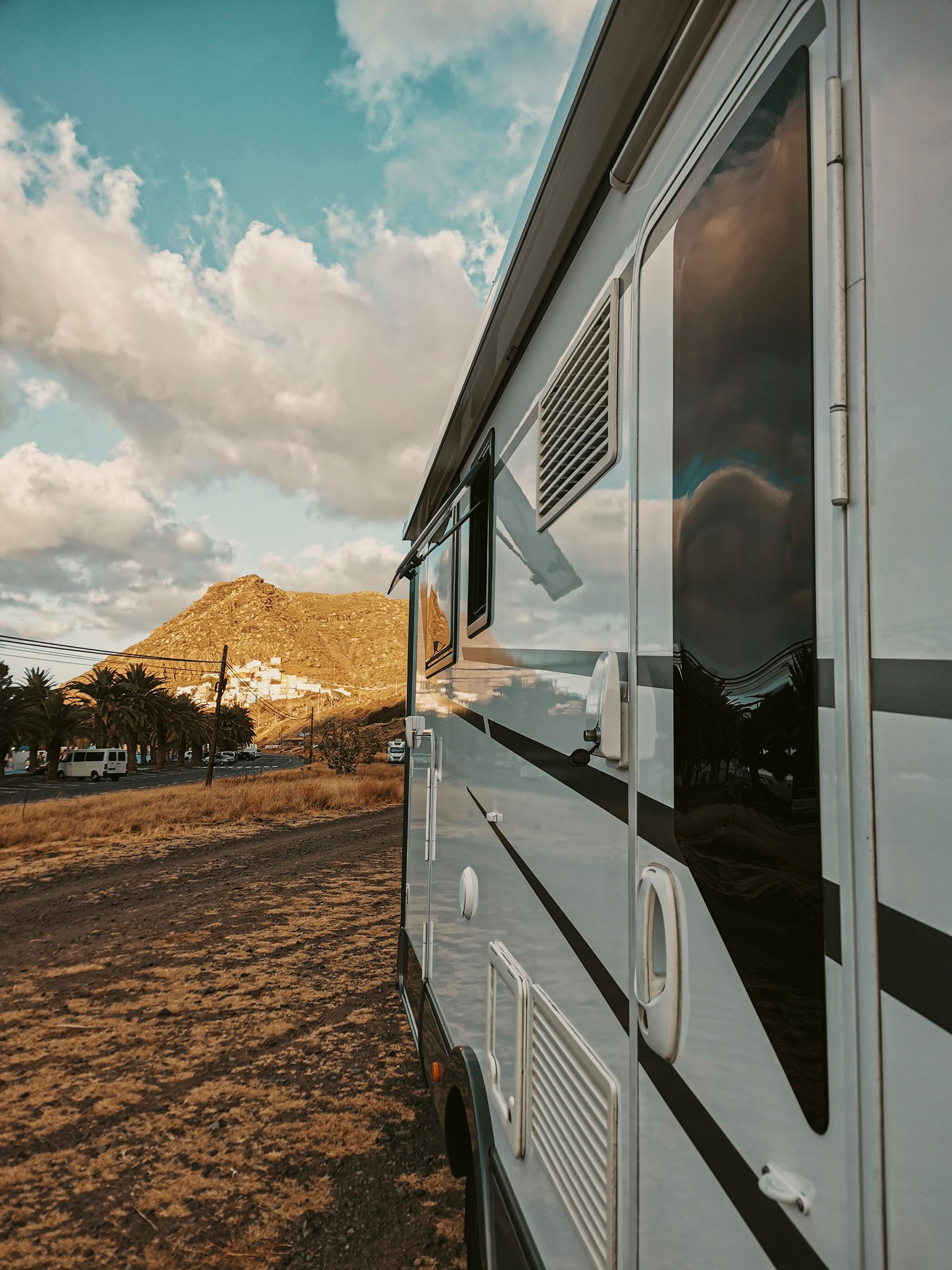 White RV beside a dirt road at sunset, with cloudy sky and golden light on distant hills