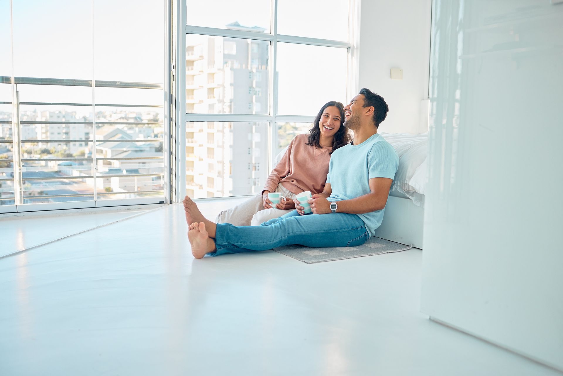 Two people sitting on the floor by a bright window, smiling and talking in a modern room
