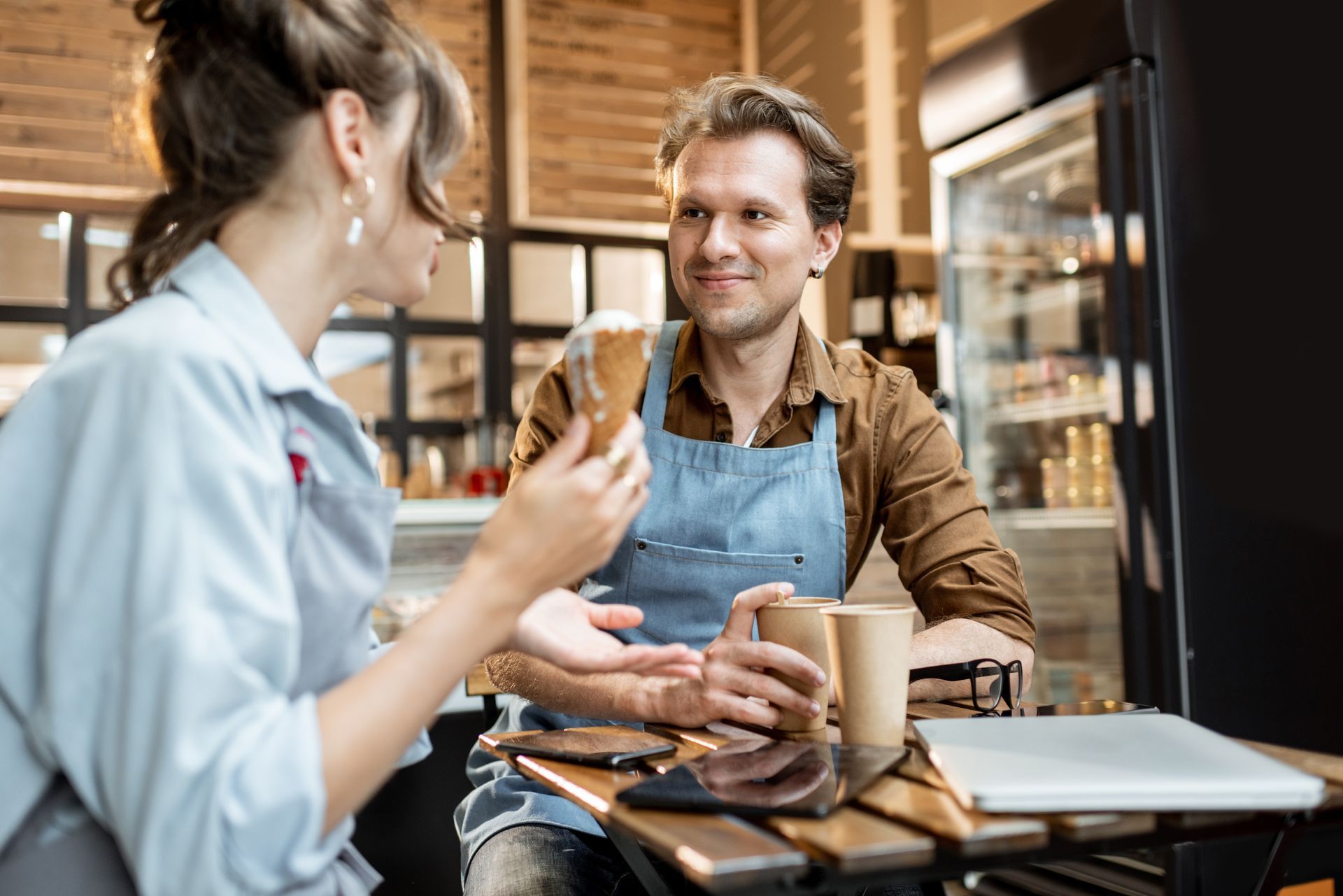 Customer and barista chatting in a café, holding coffee and smiling across a small table.