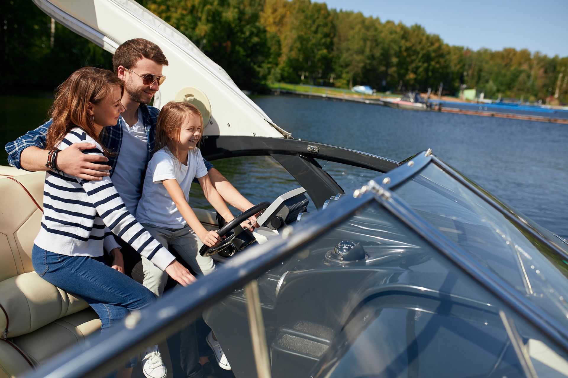 Family riding in a motorboat on a lake, with a child steering and trees along the shore in the background