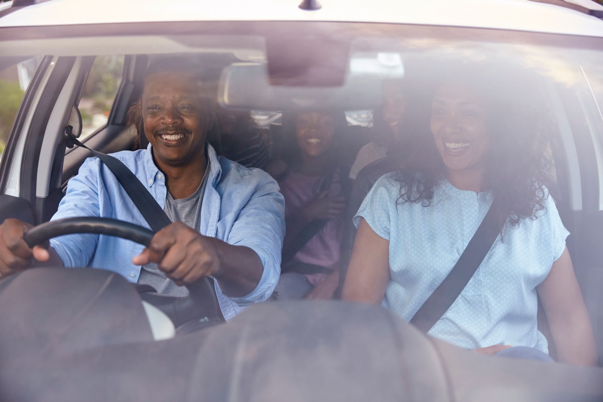 Two people in a car, one driving and one in the passenger seat, both wearing seat belts and smiling.