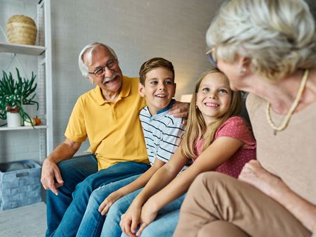Four people sitting together on a couch, smiling in a bright living room.