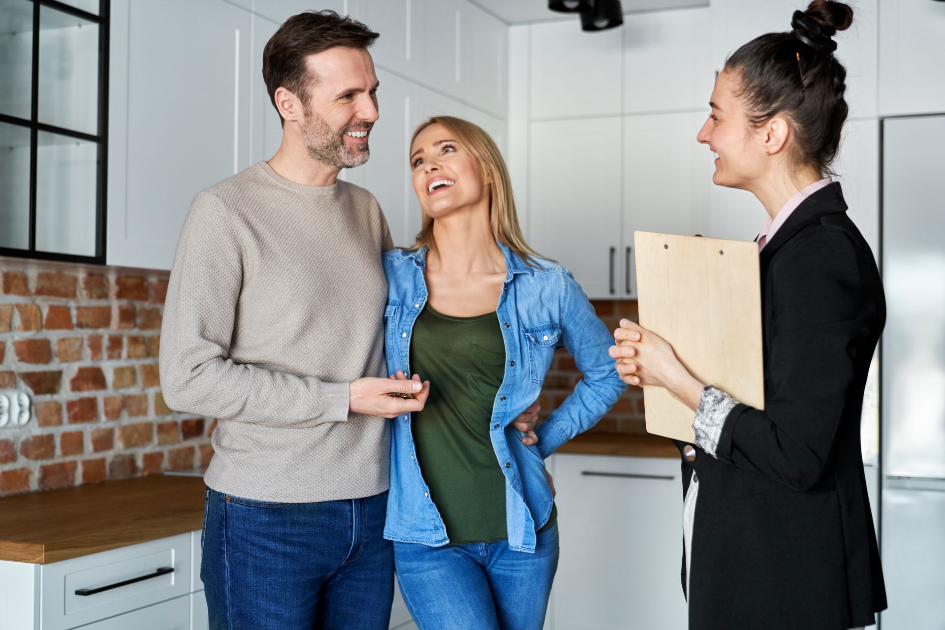 Two people talking with a smiling real estate agent in a bright kitchen