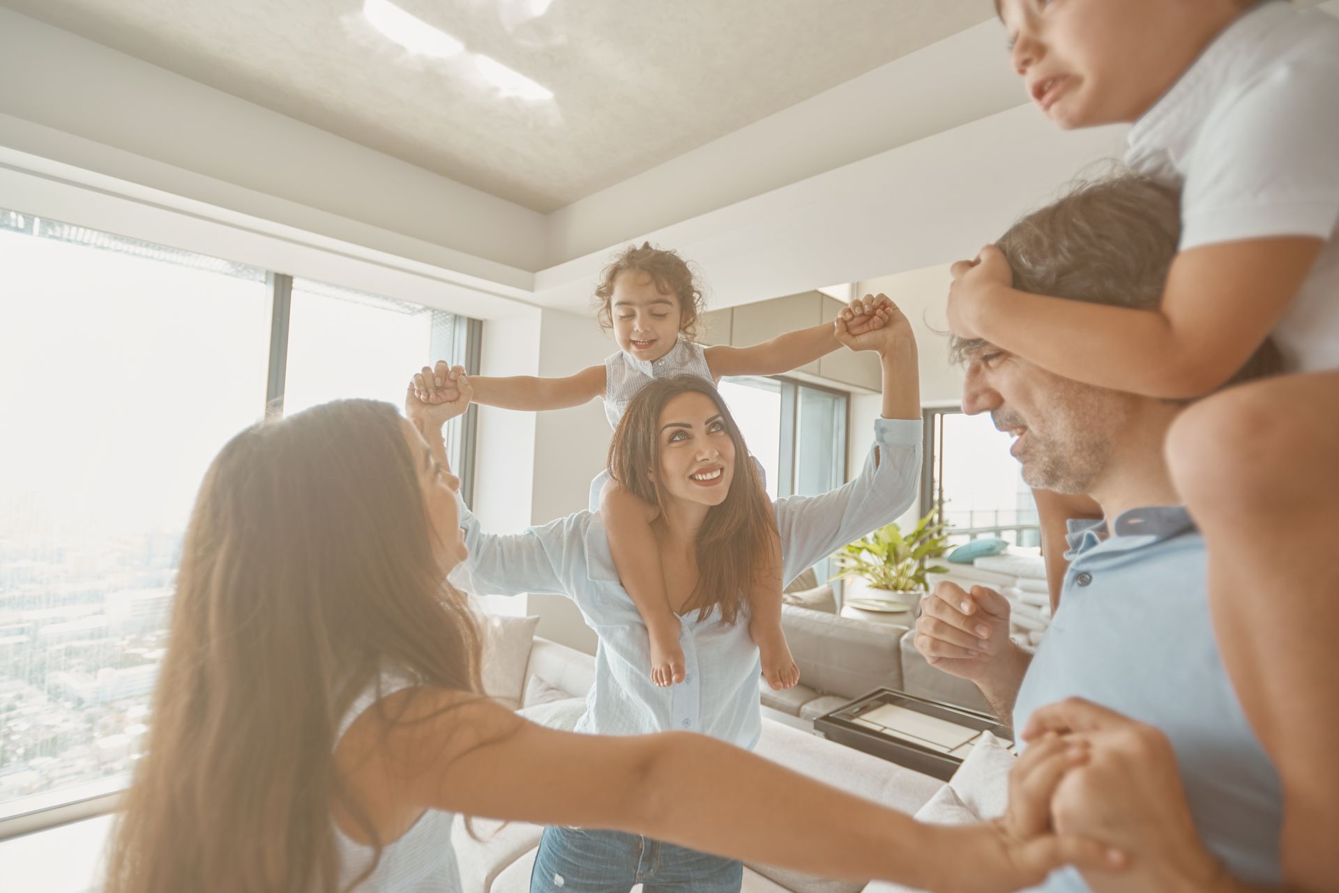 Friends laughing together in a bright living room with city views, raising their arms in celebration