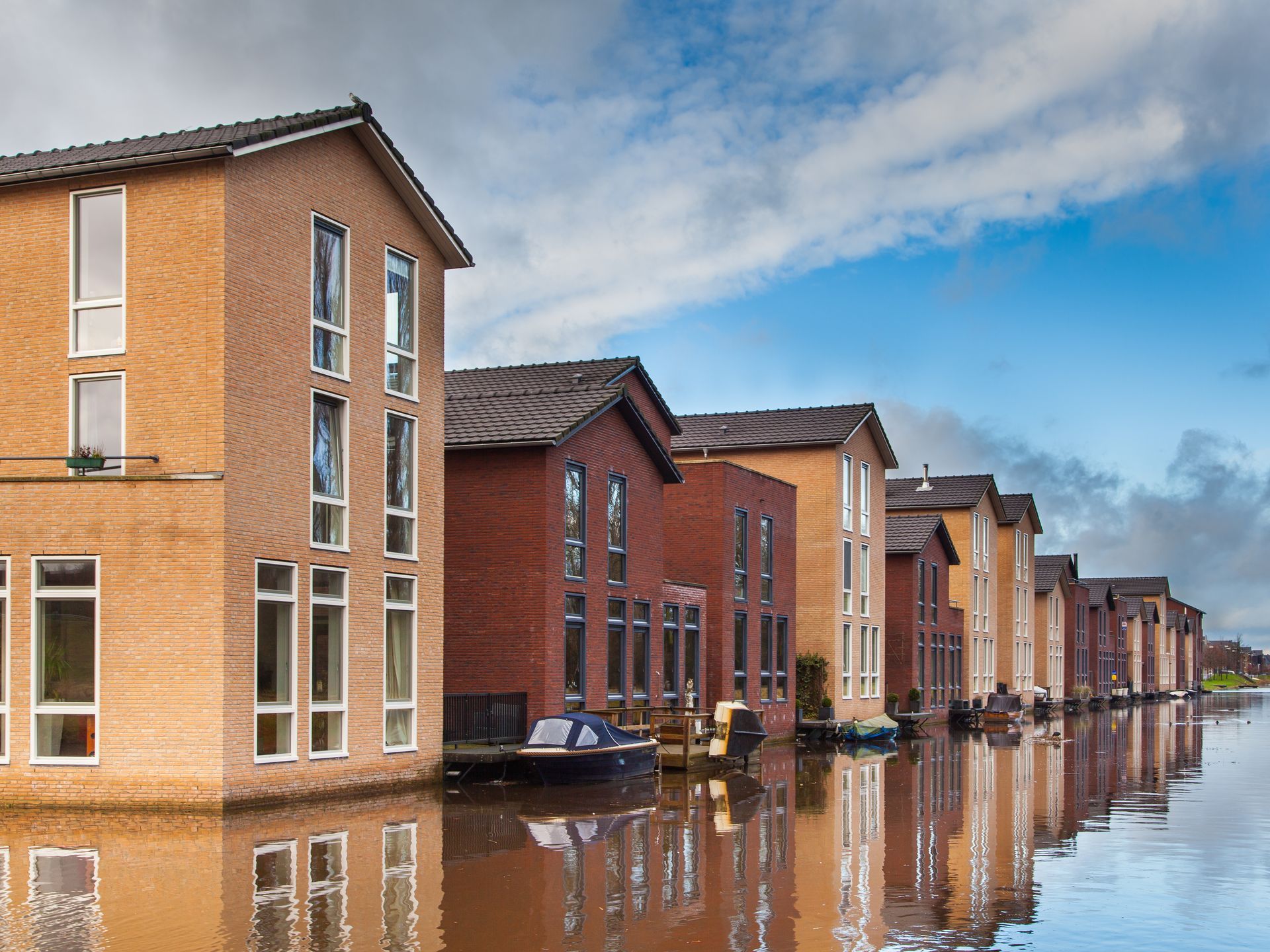 Canal-side brick apartment buildings reflected in calm water under a cloudy sky