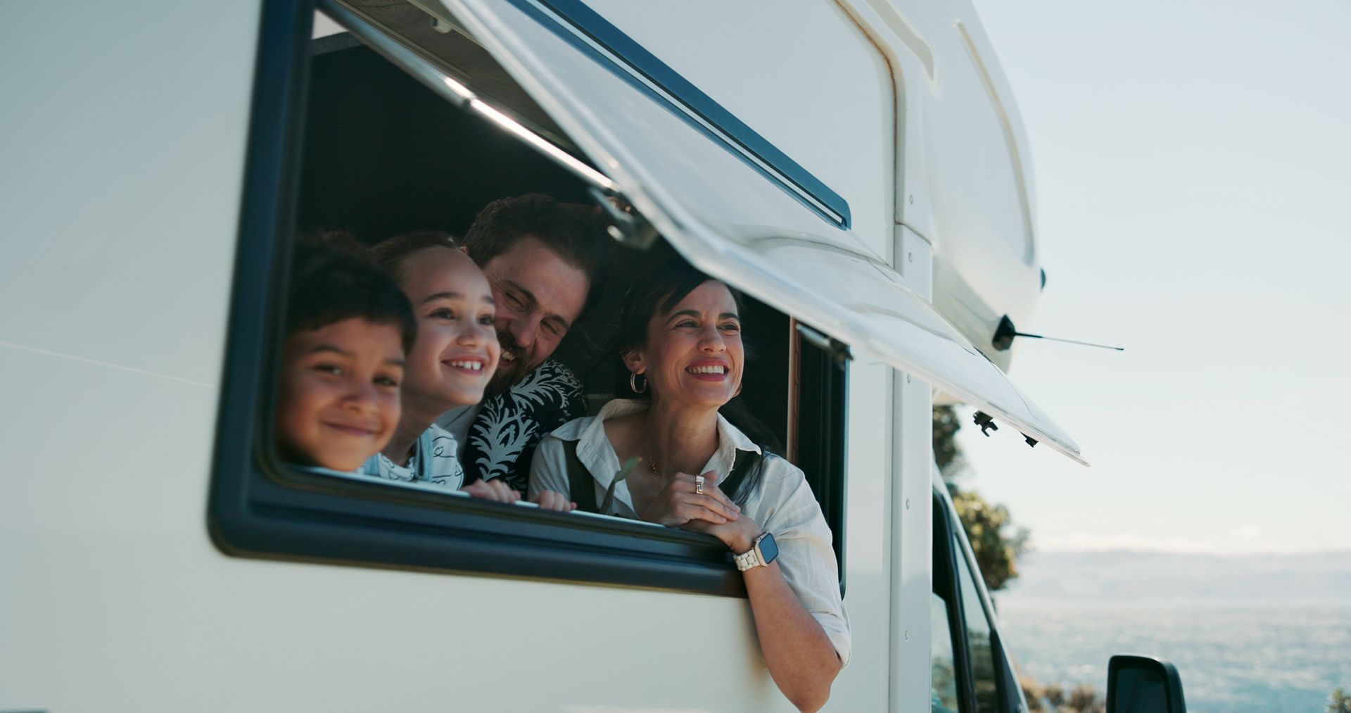People smiling and leaning out of a white camper window by the sea