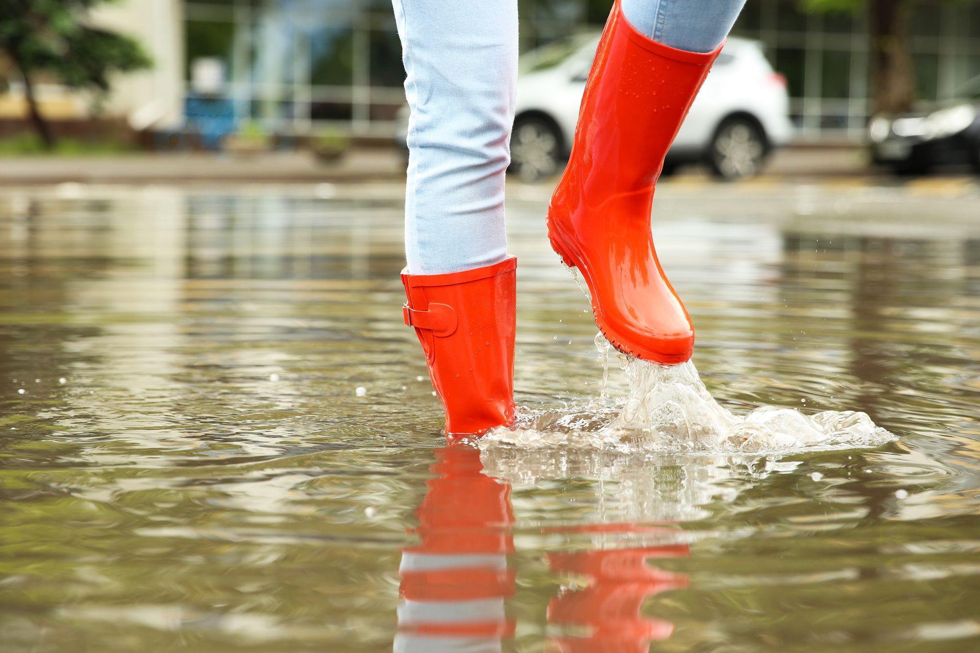 Person wearing bright red rain boots walking through a flooded street, splashing water.