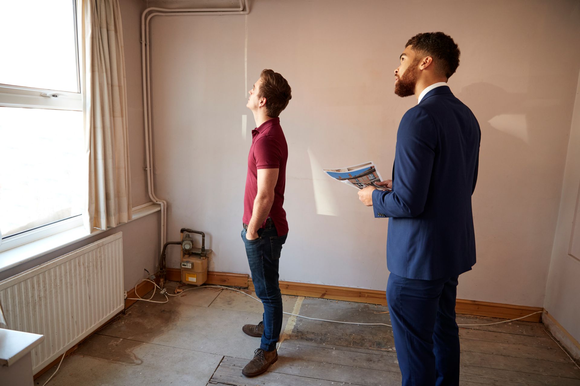Two men inspecting an empty room, one holding a clipboard by a window