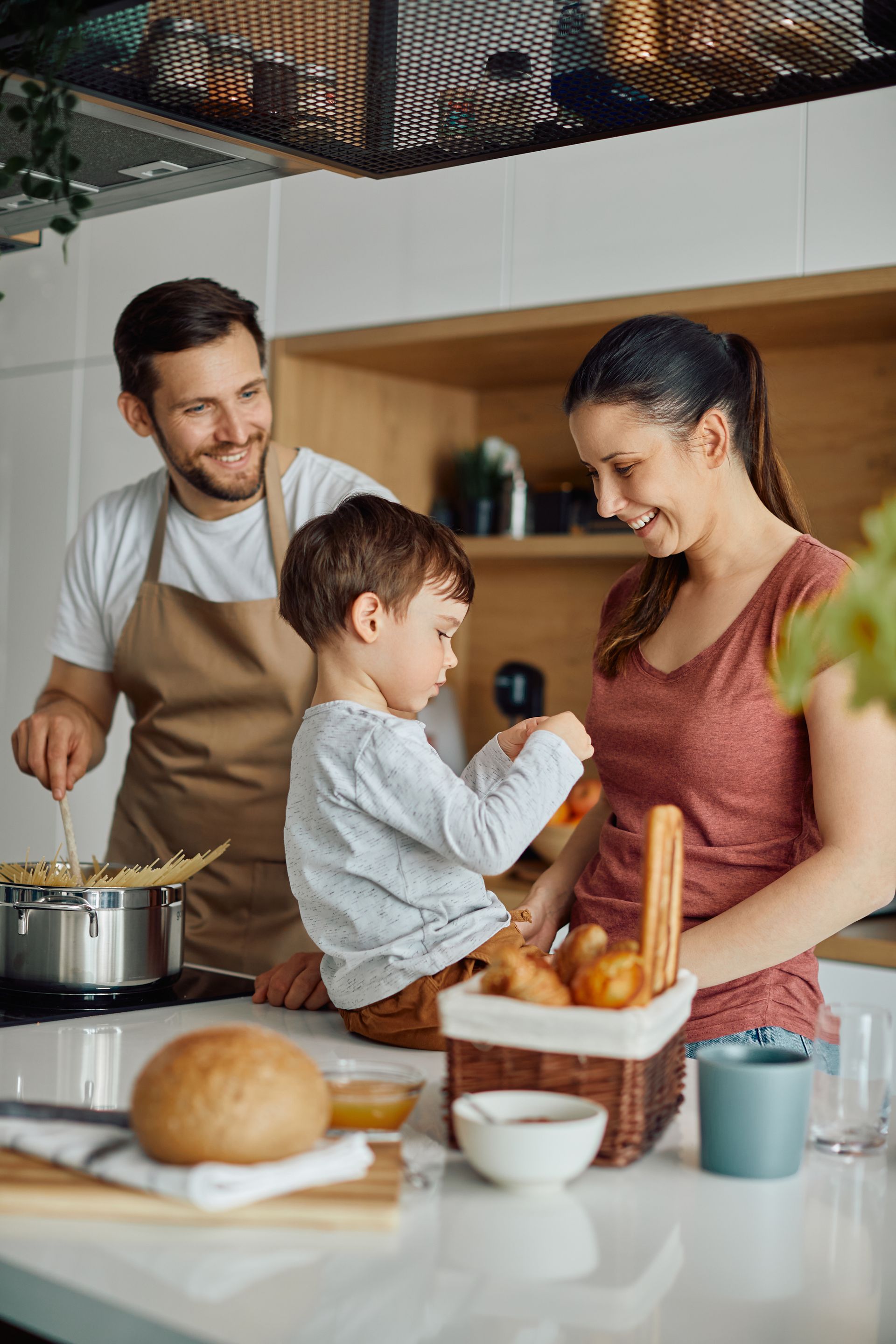 Family baking in a kitchen, smiling as a child stirs ingredients with two adults nearby.