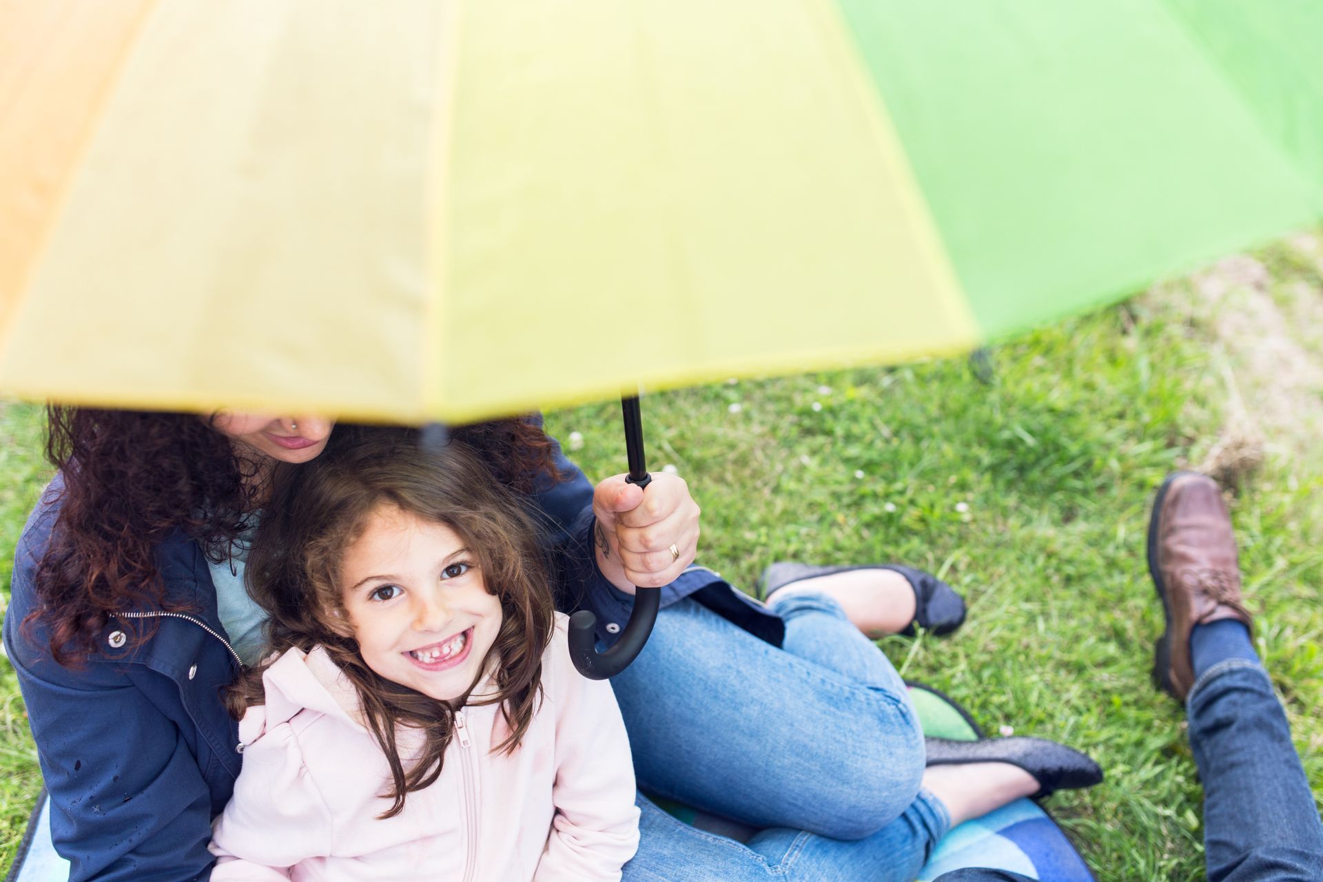 Two smiling children under a colorful umbrella sitting on grass outdoors