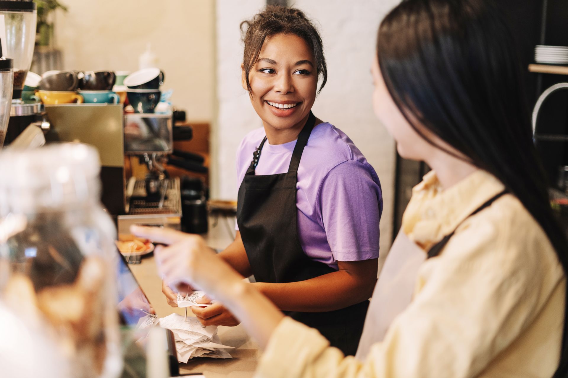 Barista in a black apron smiles while serving a customer at a café counter