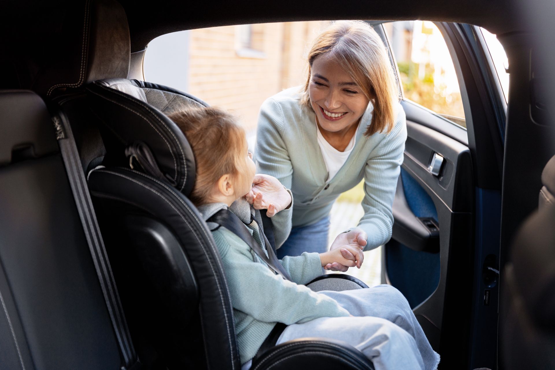 Woman smiling and handing something to a child seated in a car back seat