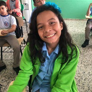 A girl in a green jacket is smiling in a classroom