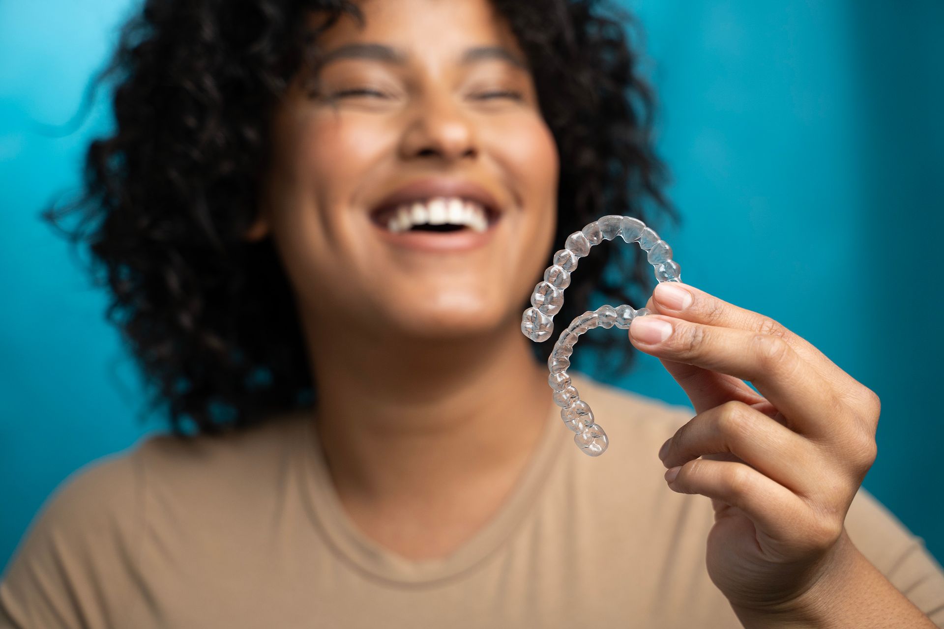 A woman is holding a pair of clear braces in her hands and smiling.