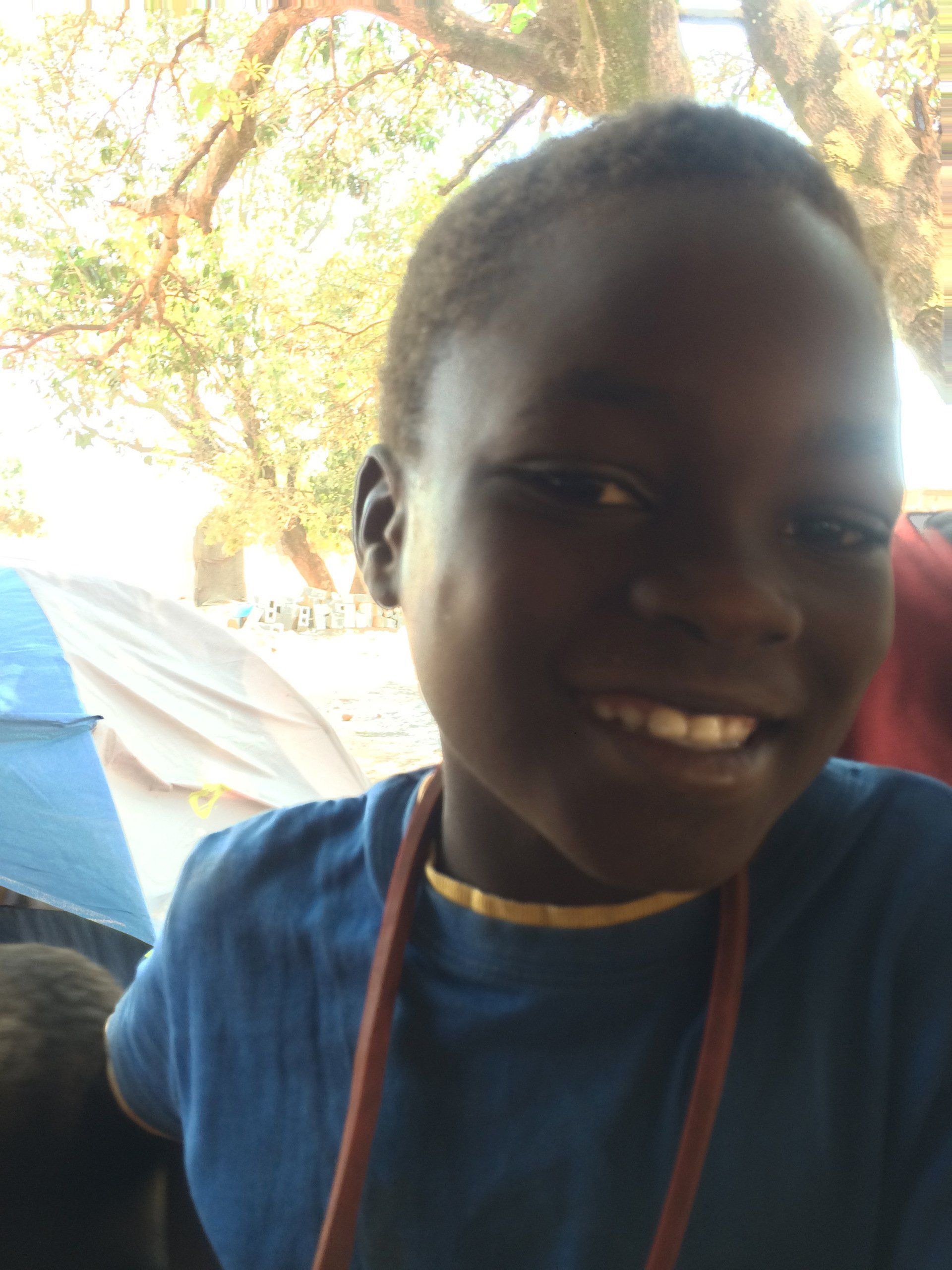 A young boy in a blue shirt is smiling for the camera