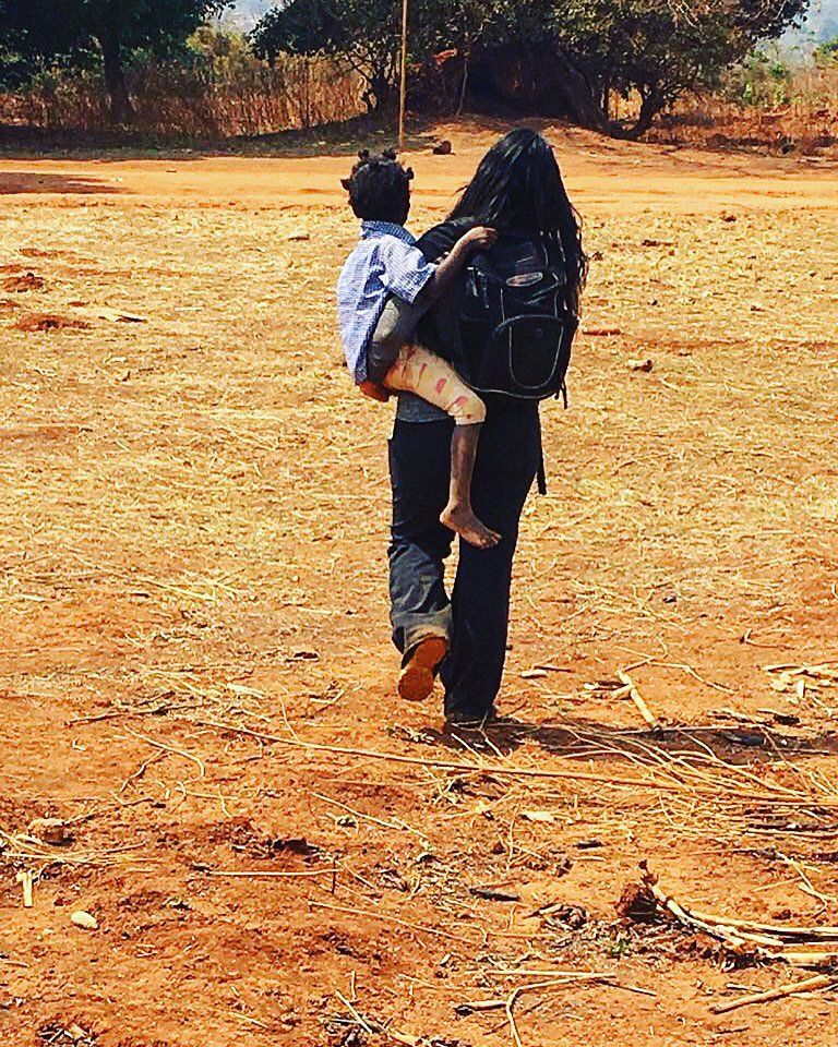 A woman is carrying a child on her back in a field