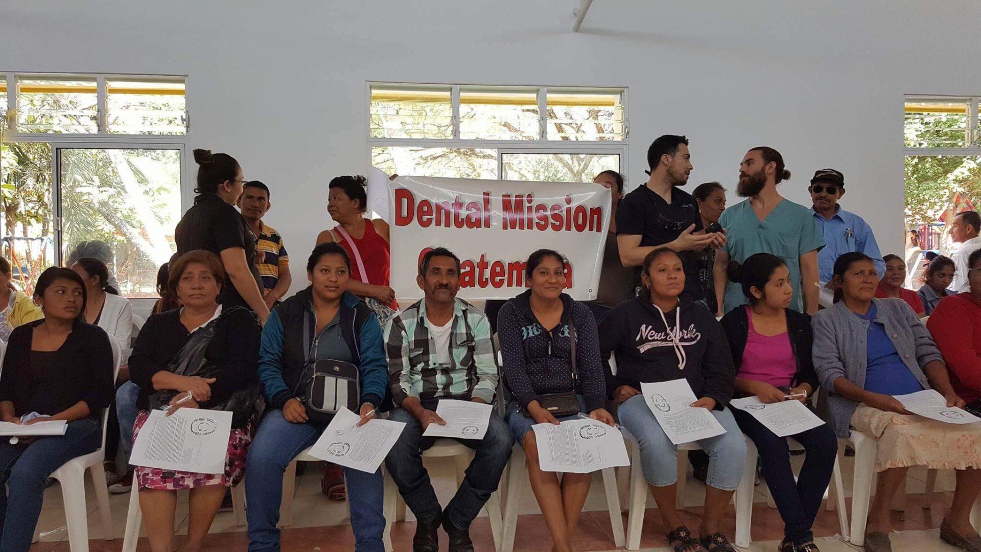 A group of people are sitting in chairs in front of a sign that says denial mission
