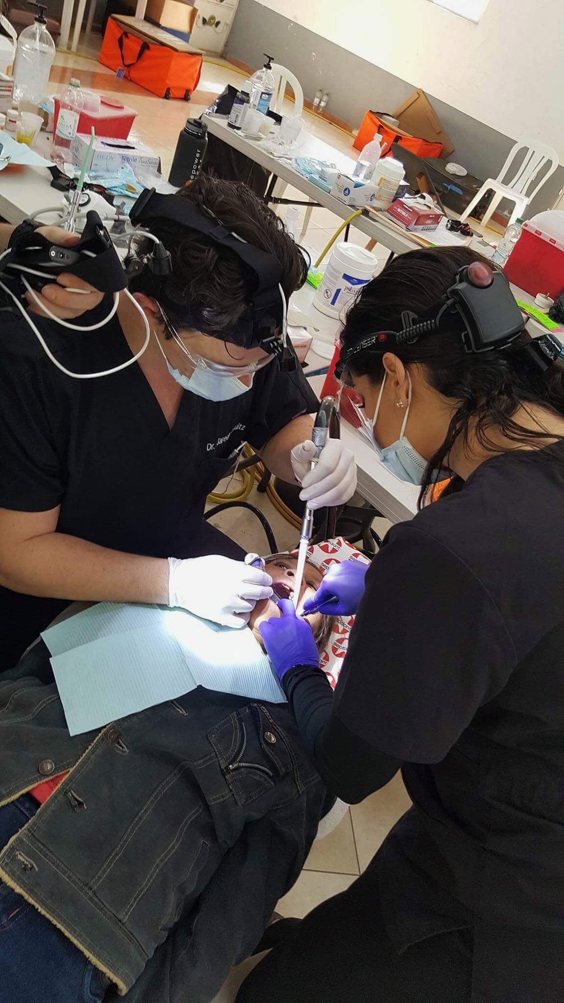 Two dentists are working on a patient 's teeth in a dental office.