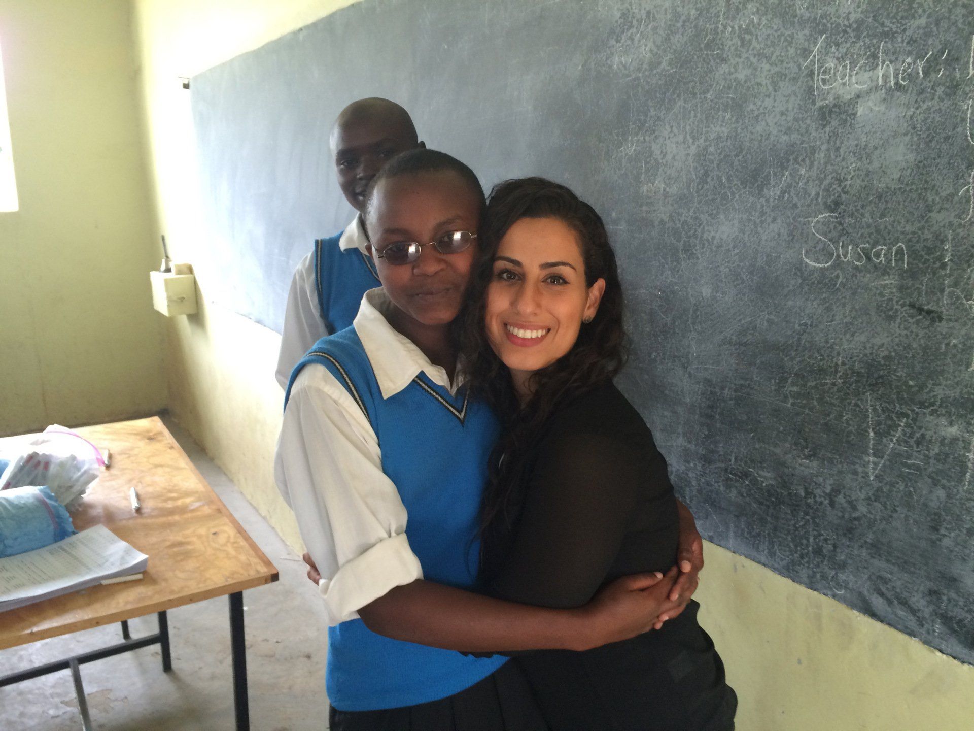A woman is hugging a girl in front of a blackboard that says 