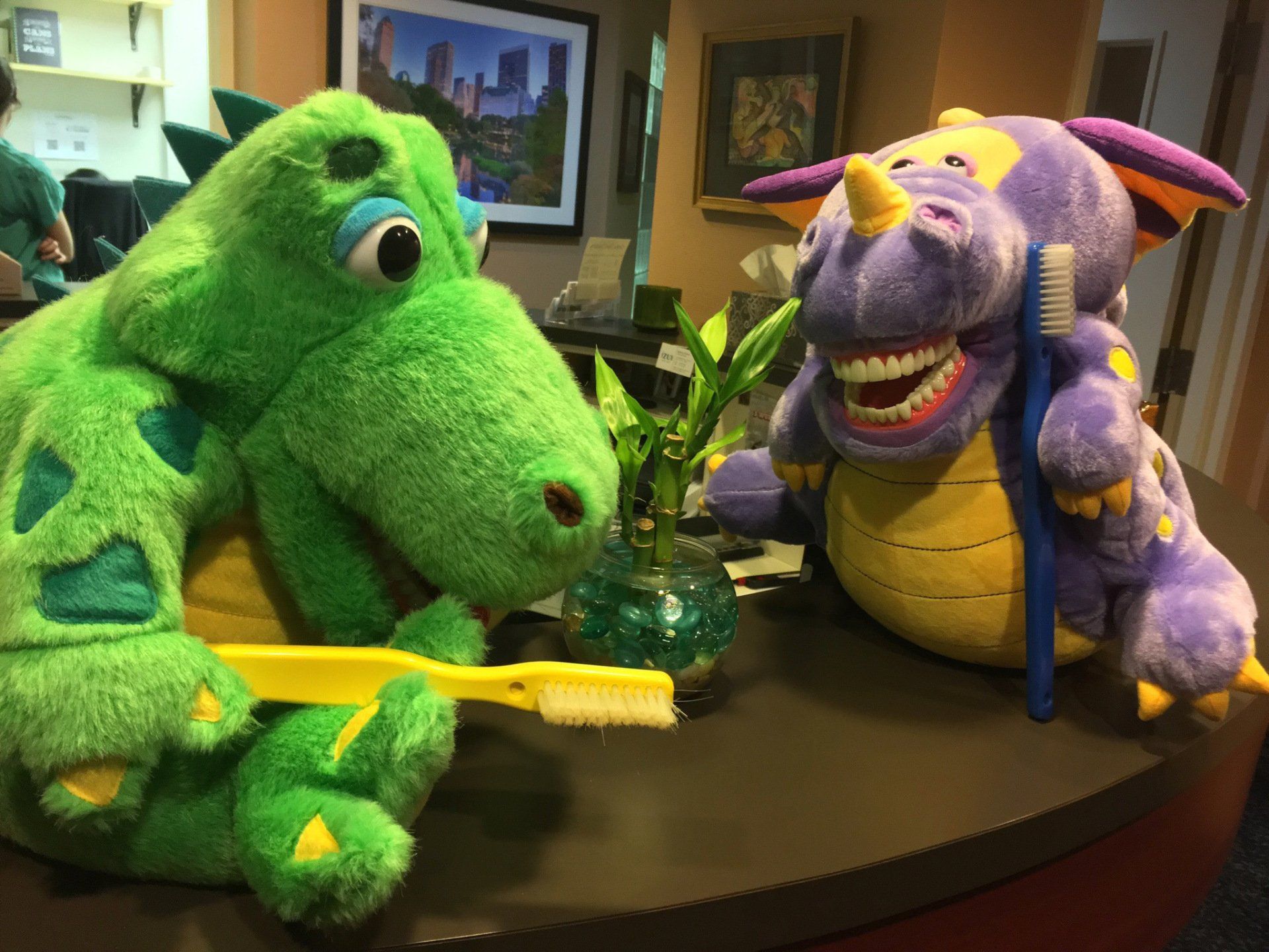 Two stuffed dinosaurs are brushing their teeth on a table.
