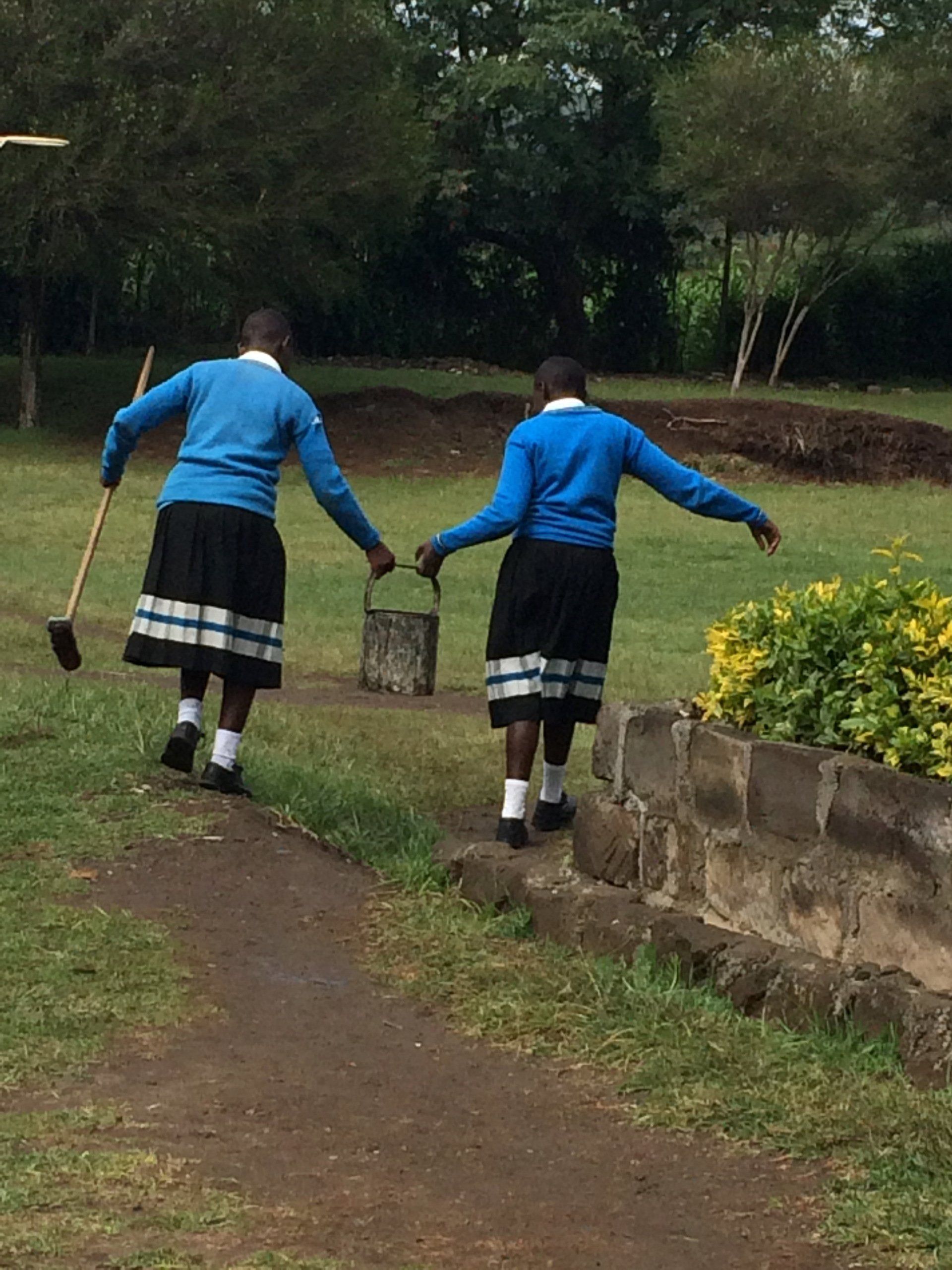 Two girls in school uniforms are walking down a path