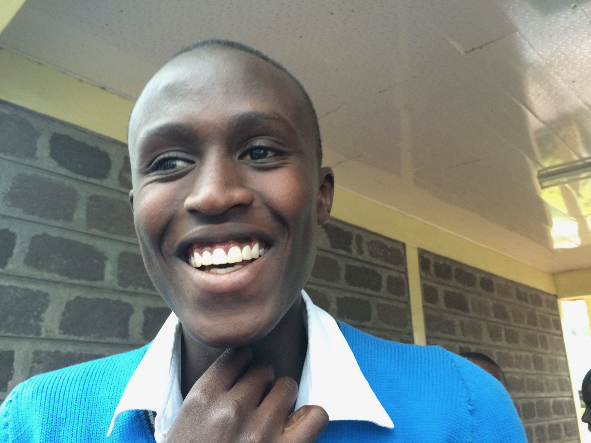A man in a blue sweater is smiling with his hand on his neck