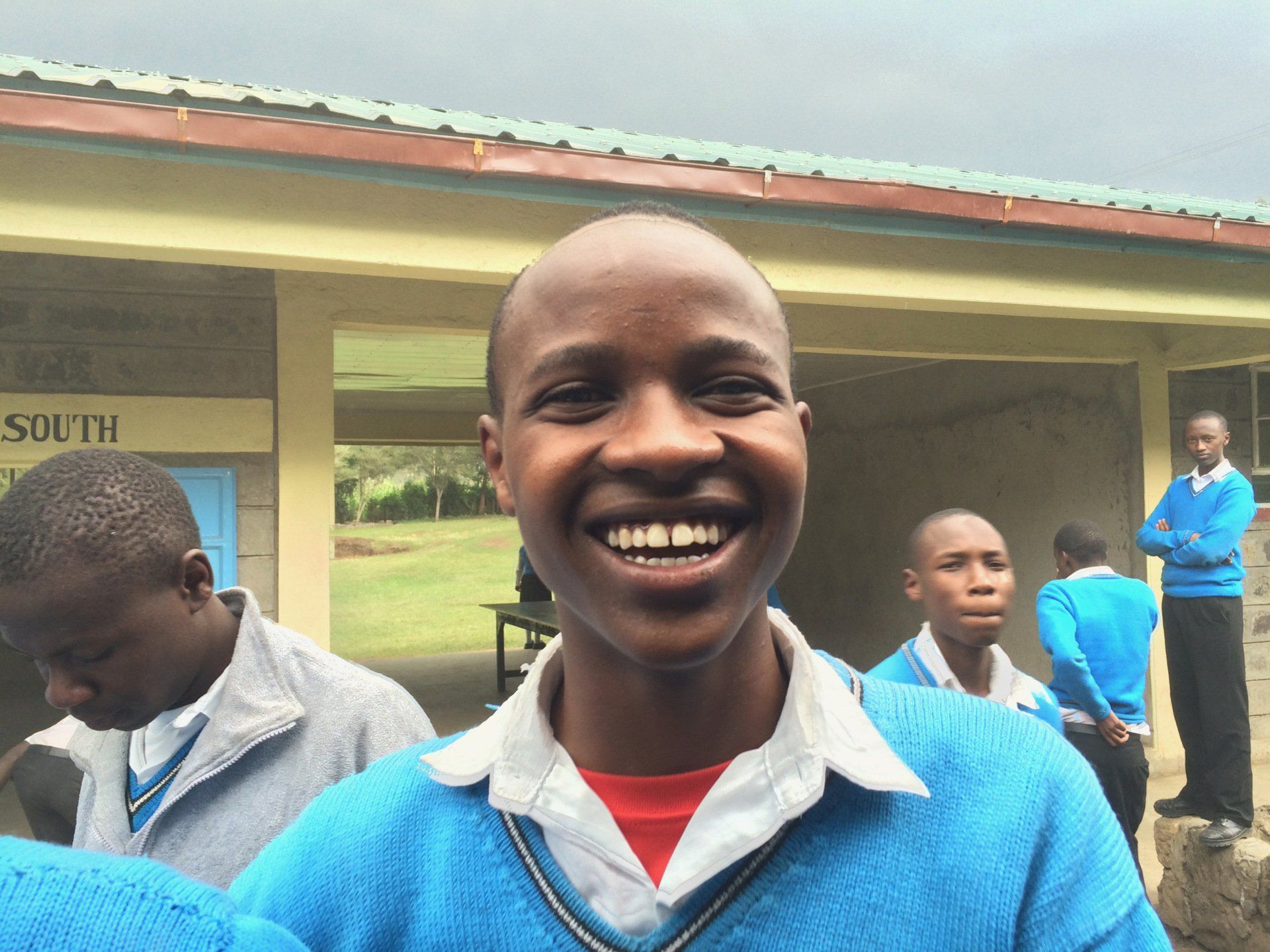 A boy in a blue sweater is smiling in front of a building that says south