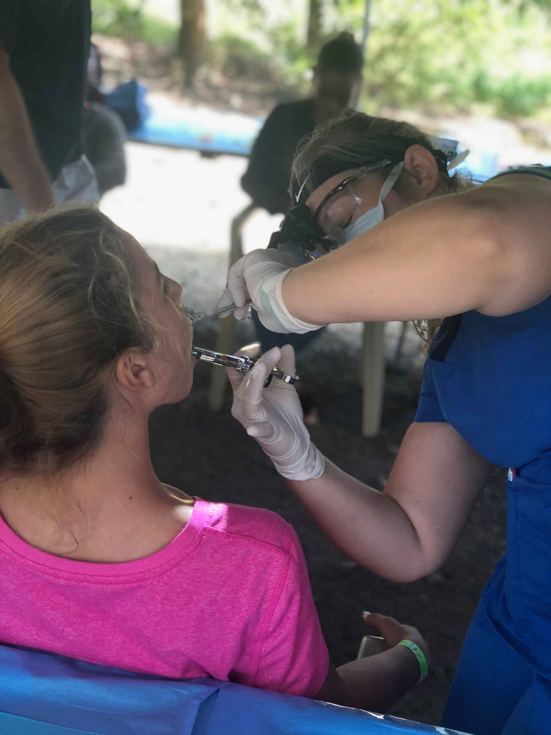 A woman in a pink shirt is getting her teeth examined by a nurse.