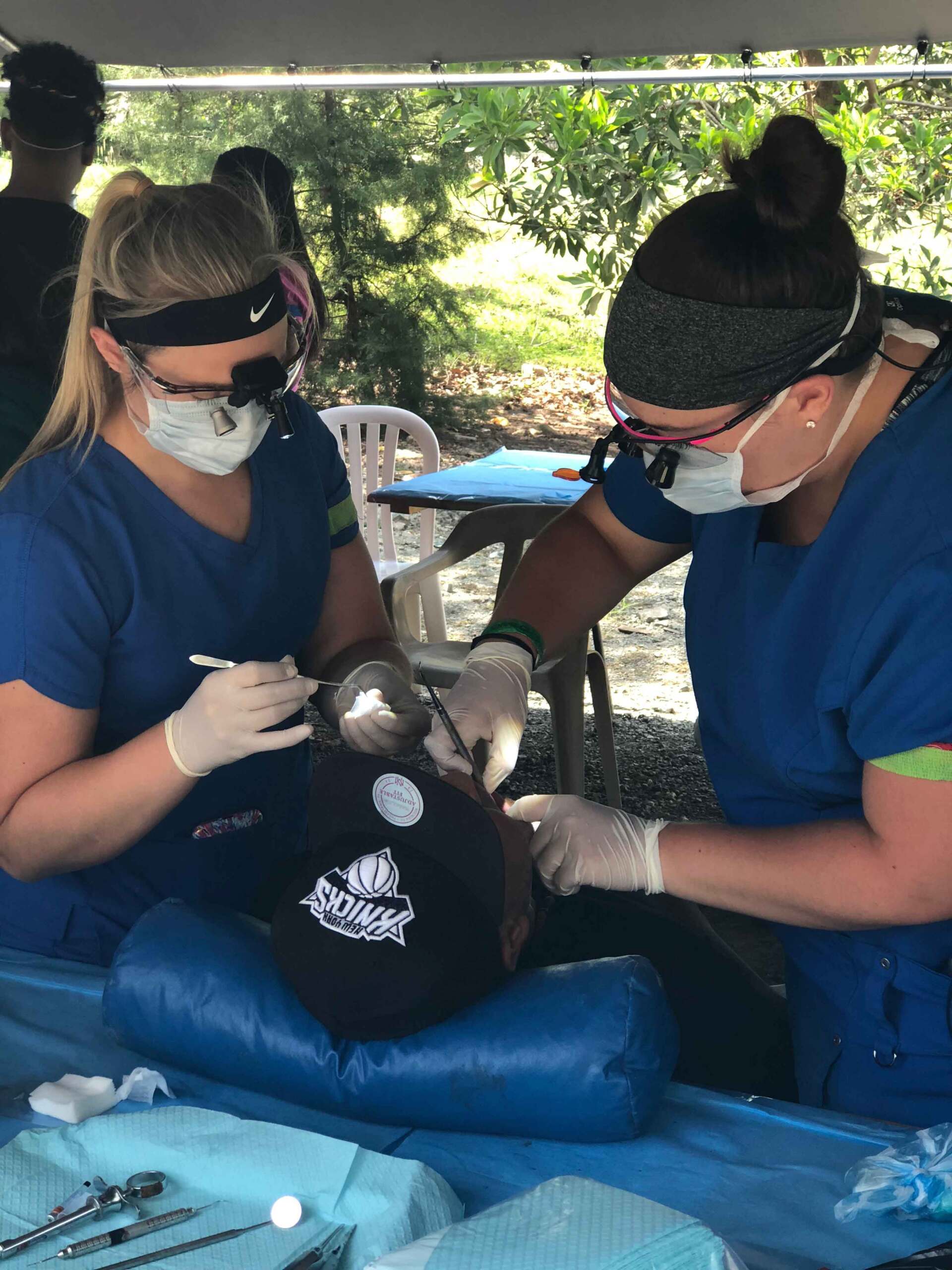Two female dentists are working on a patient 's teeth under a tent.