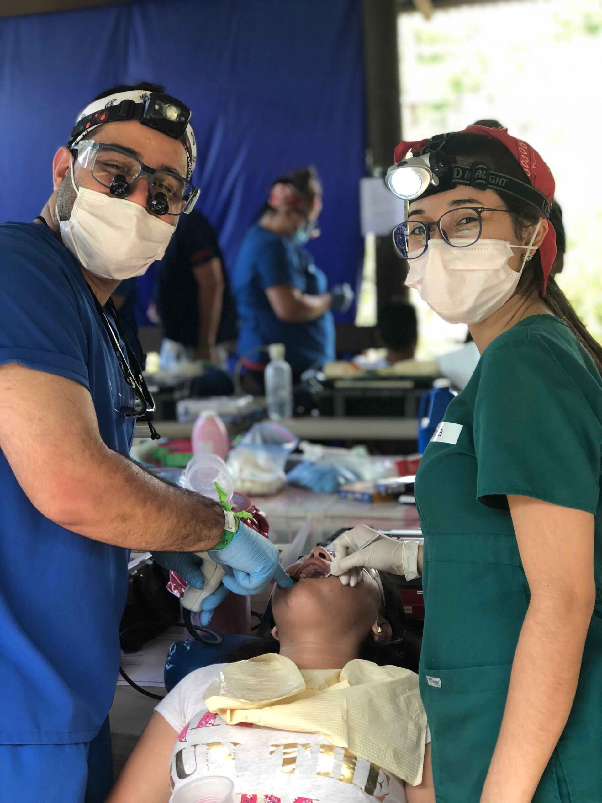 A man and a woman wearing masks are working on a patient 's teeth.
