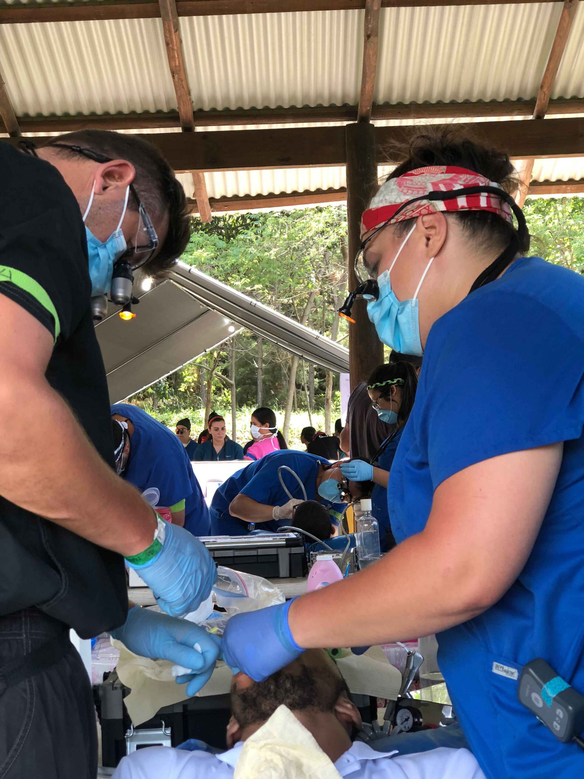 A group of dentists are working on a patient under a canopy.