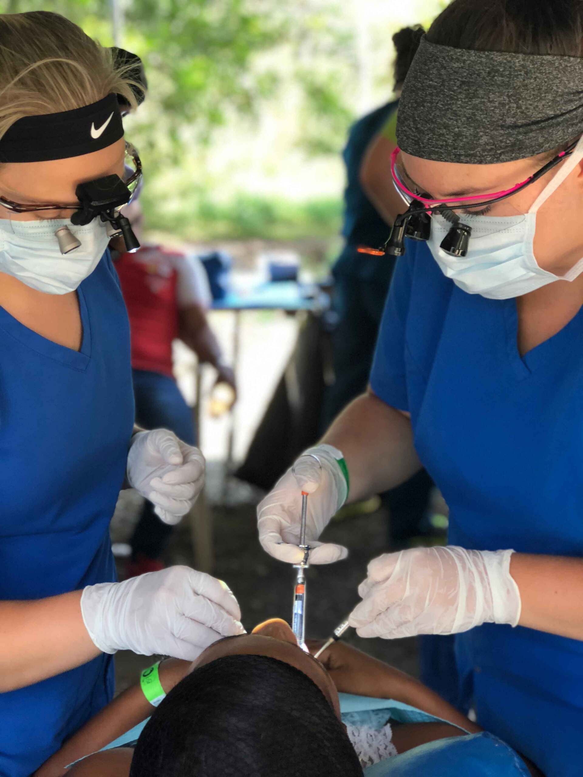 Two women in blue scrubs are working on a patient