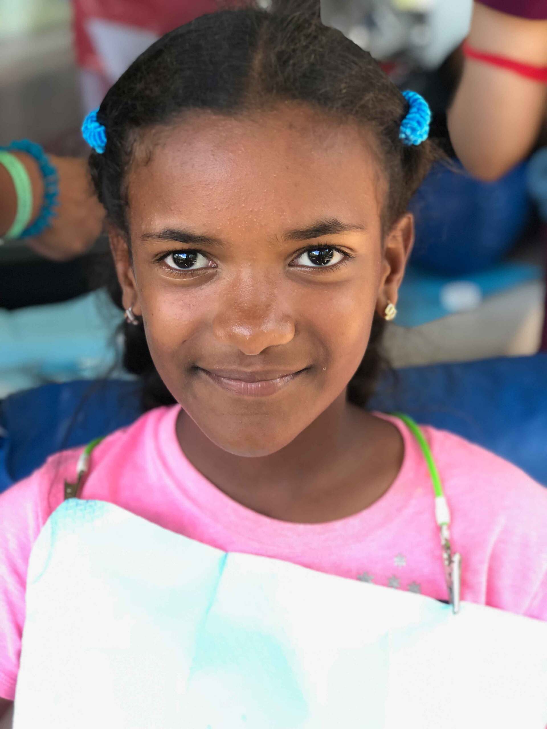 A young girl in a pink shirt is smiling for the camera.