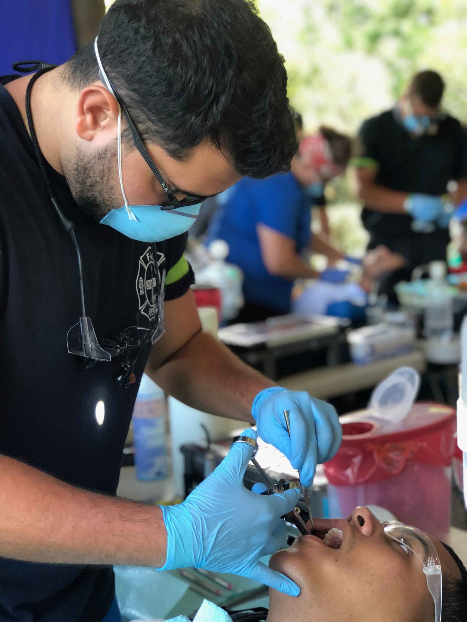 A dentist is examining a patient 's teeth while wearing a mask and gloves