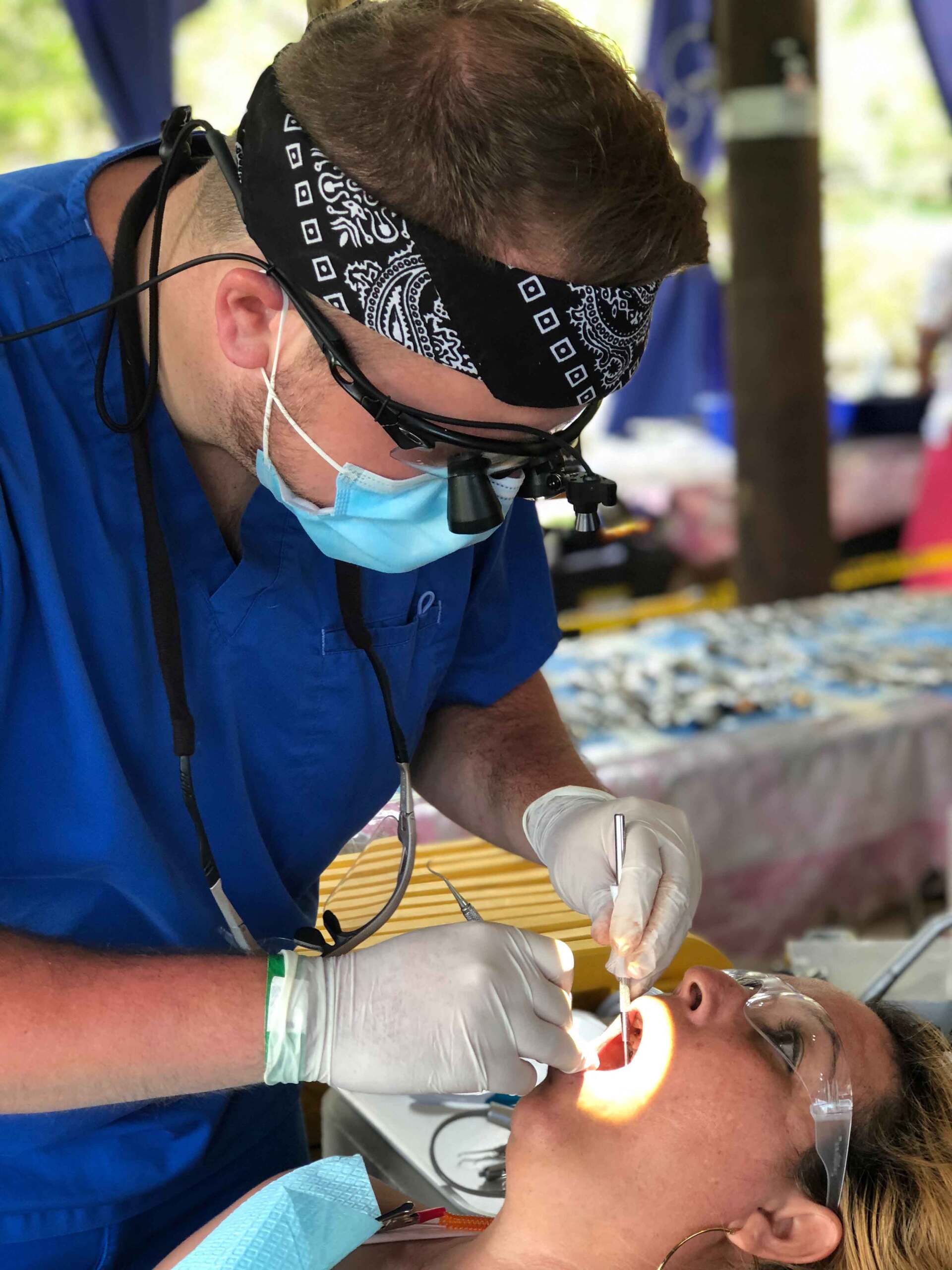 A dentist is examining a woman 's teeth while wearing a bandana