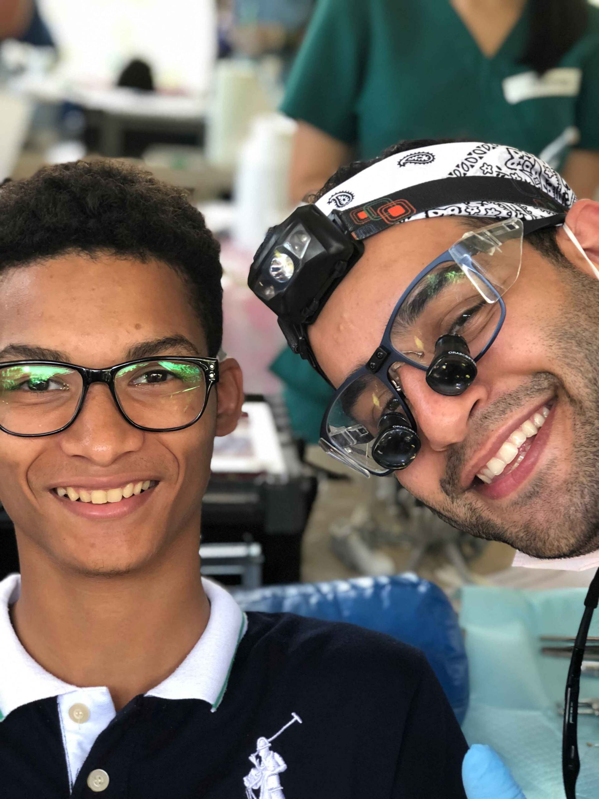 A man wearing glasses is smiling next to another man wearing glasses