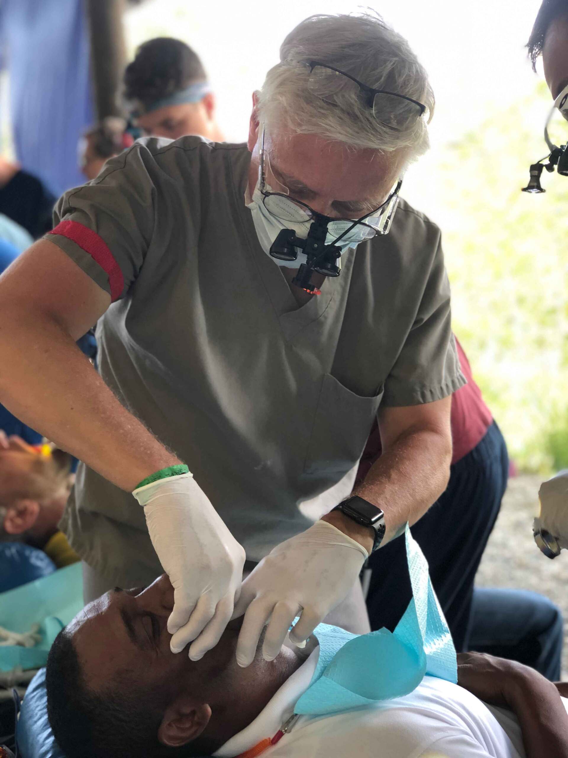 A man wearing a mask and gloves is examining a man 's teeth.