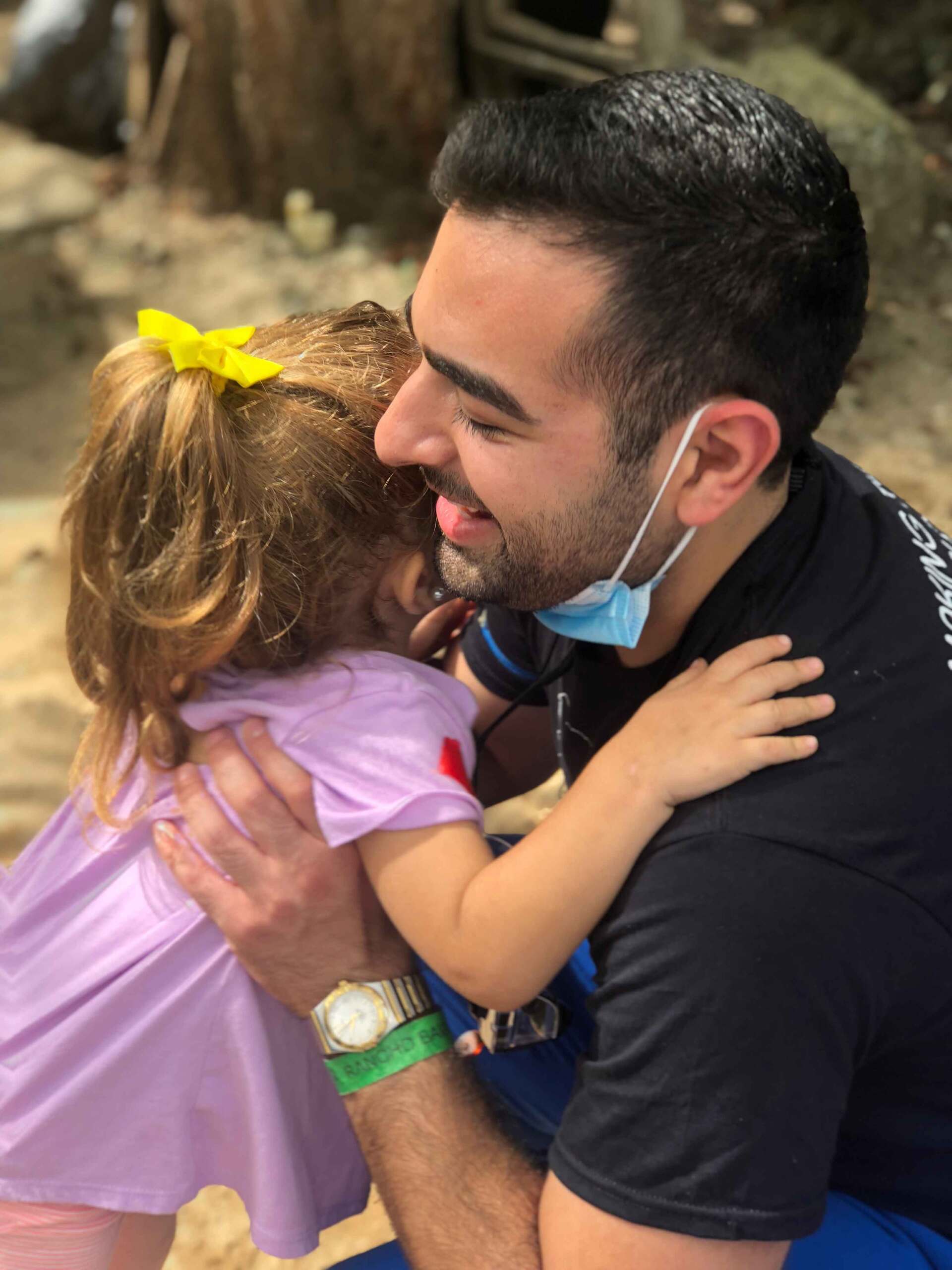 A man wearing a mask is hugging a little girl