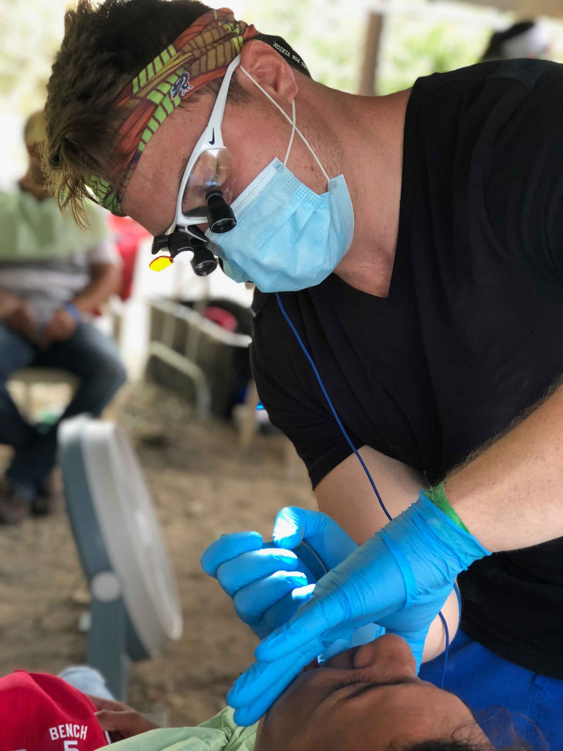 A dentist wearing a mask and blue gloves examines a patient 's teeth