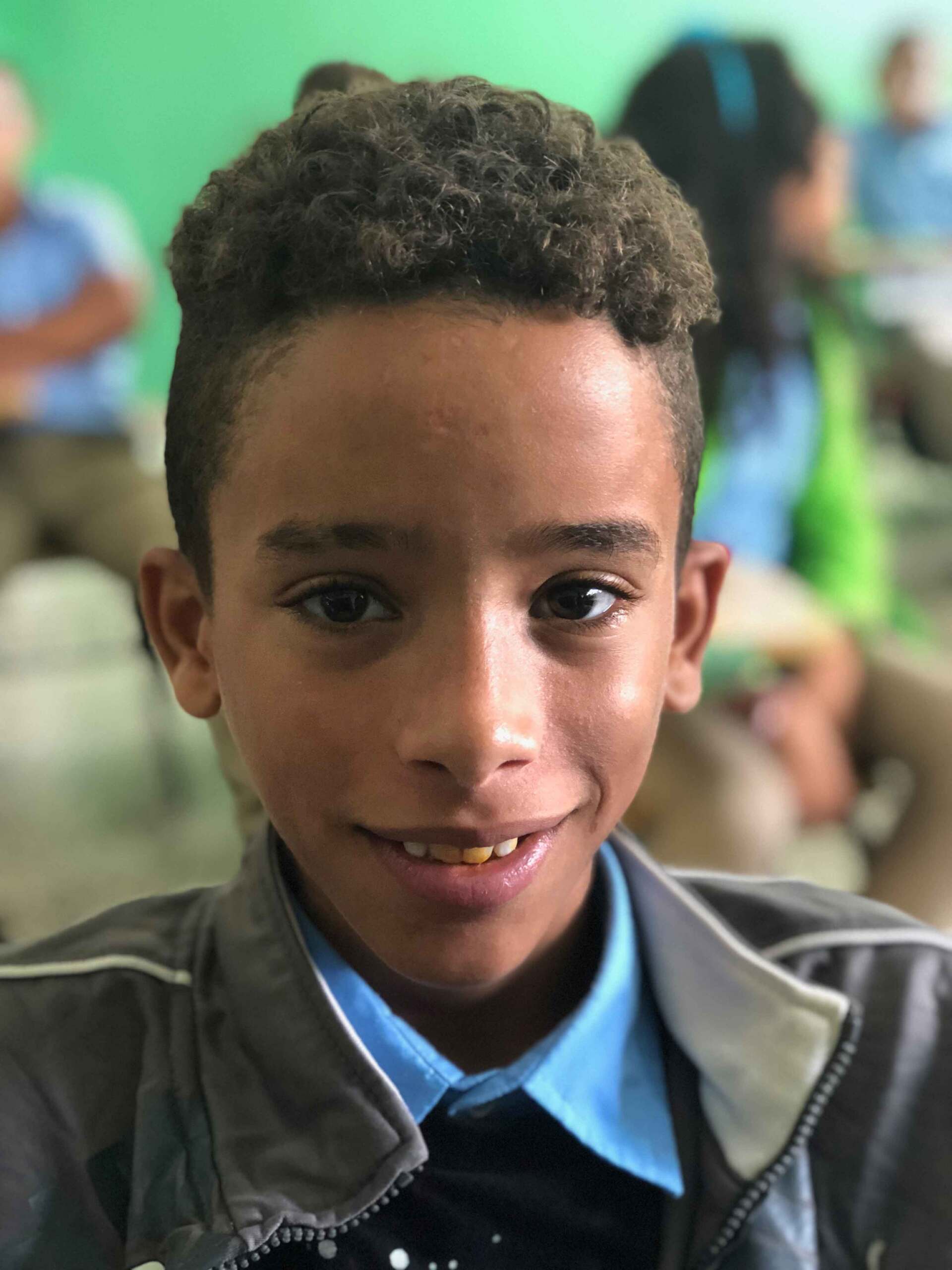 A young boy wearing a jacket and a blue shirt smiles for the camera
