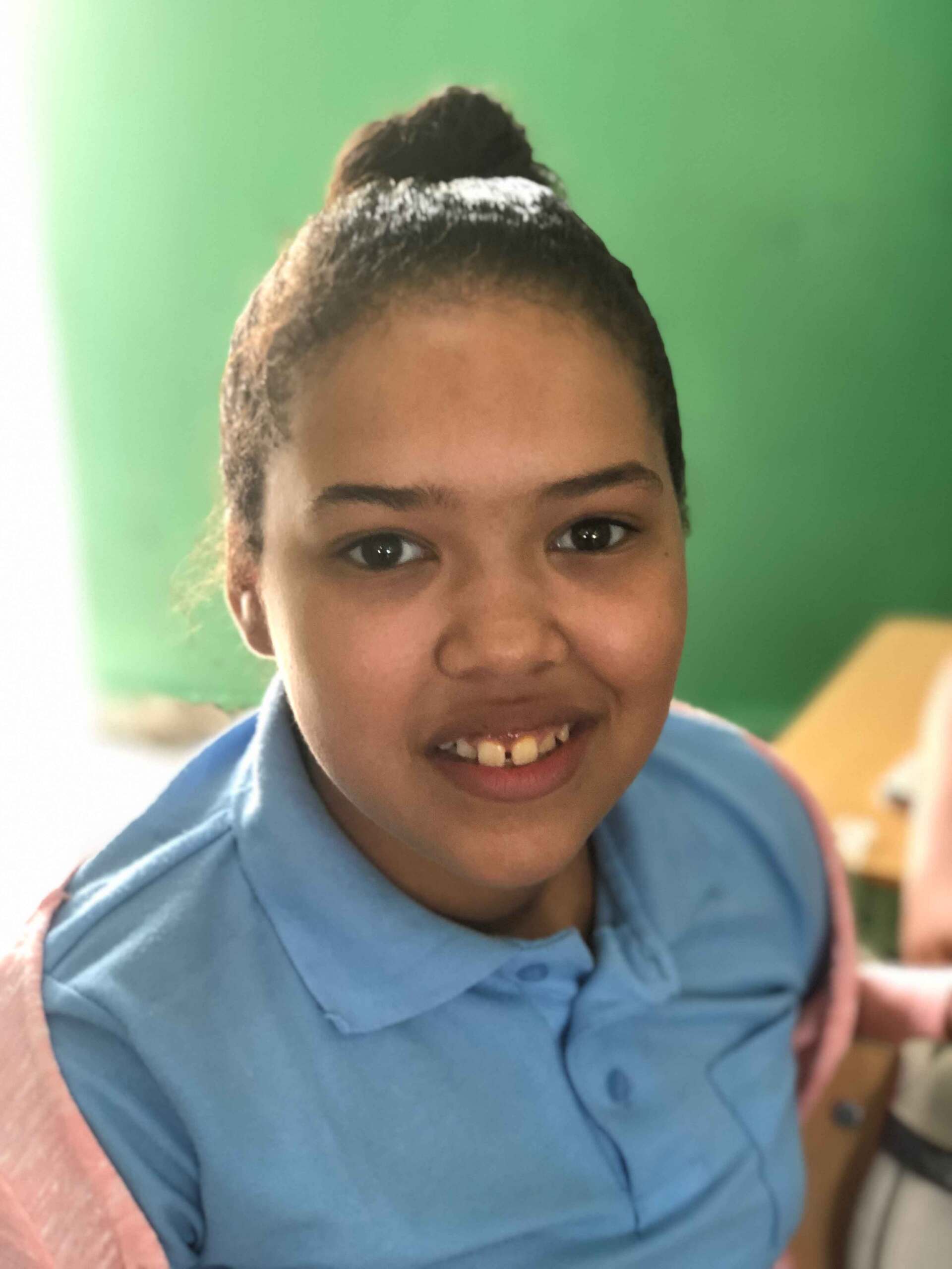 A young girl in a blue shirt is smiling for the camera