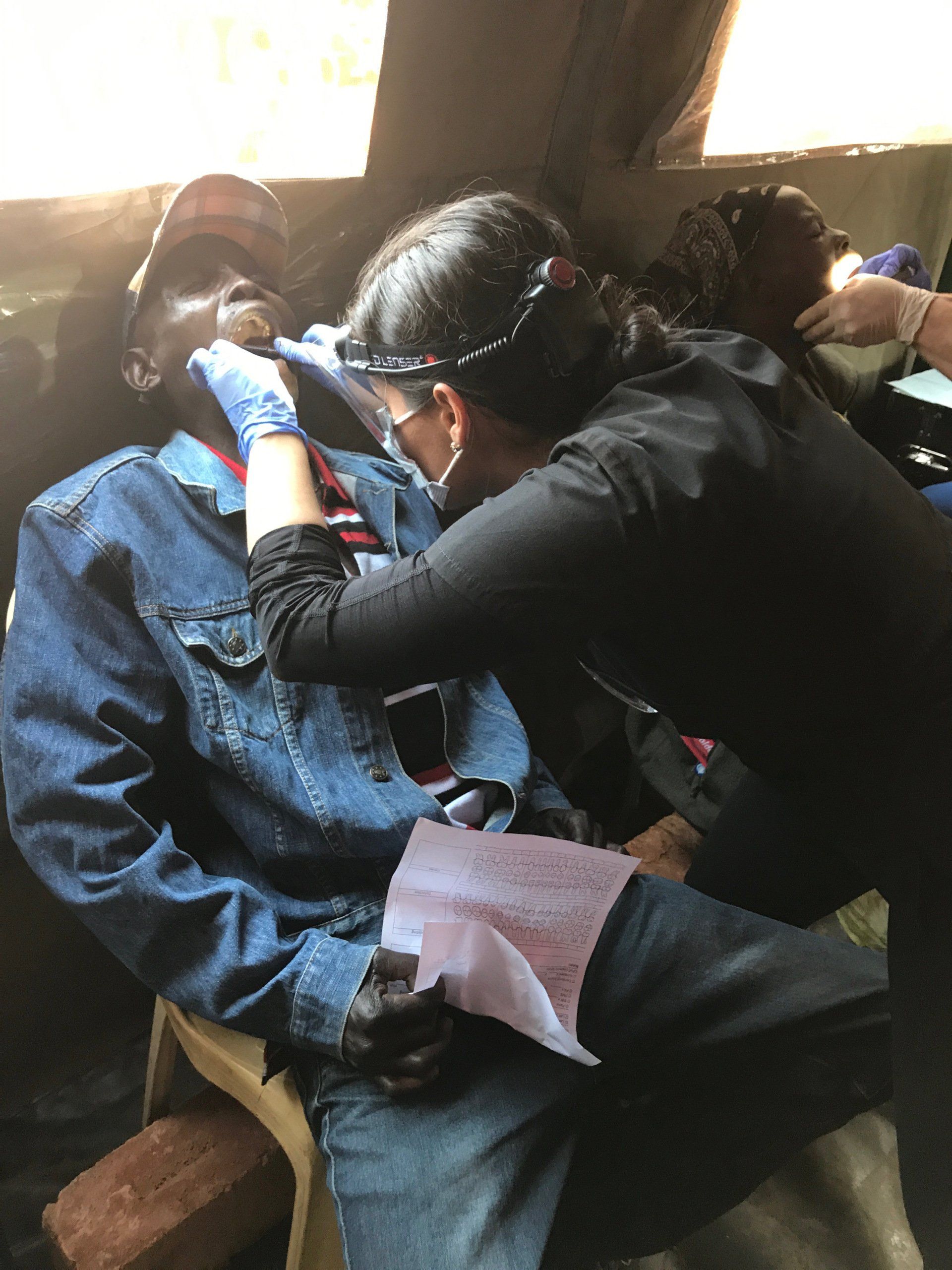A woman is examining a man 's teeth in a chair.