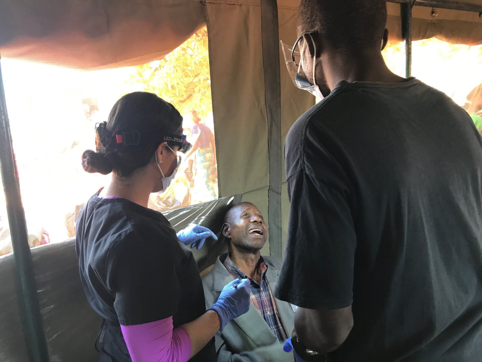 A woman is examining a man 's teeth in a tent.