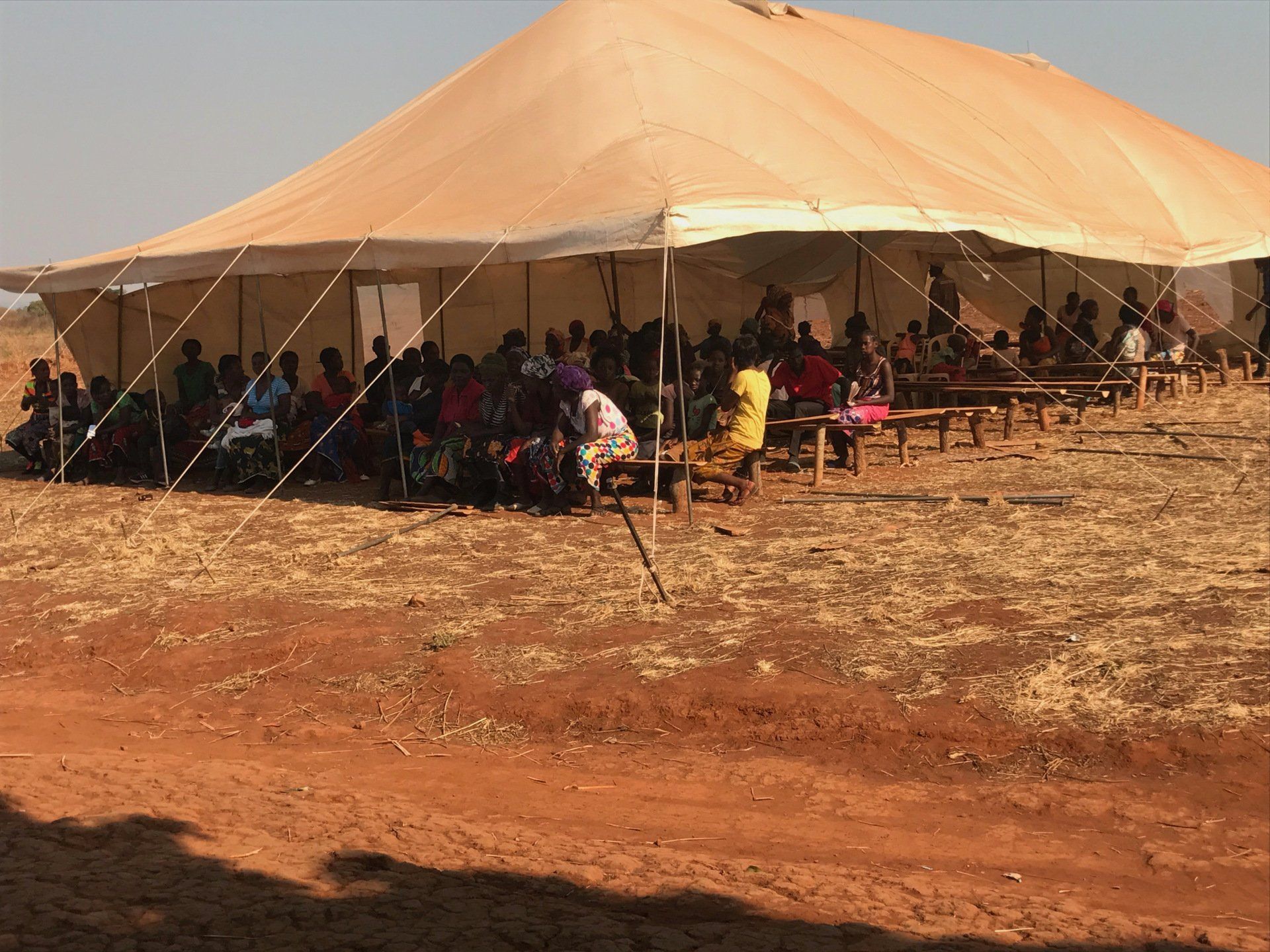 A group of people are sitting under a tent in a field.
