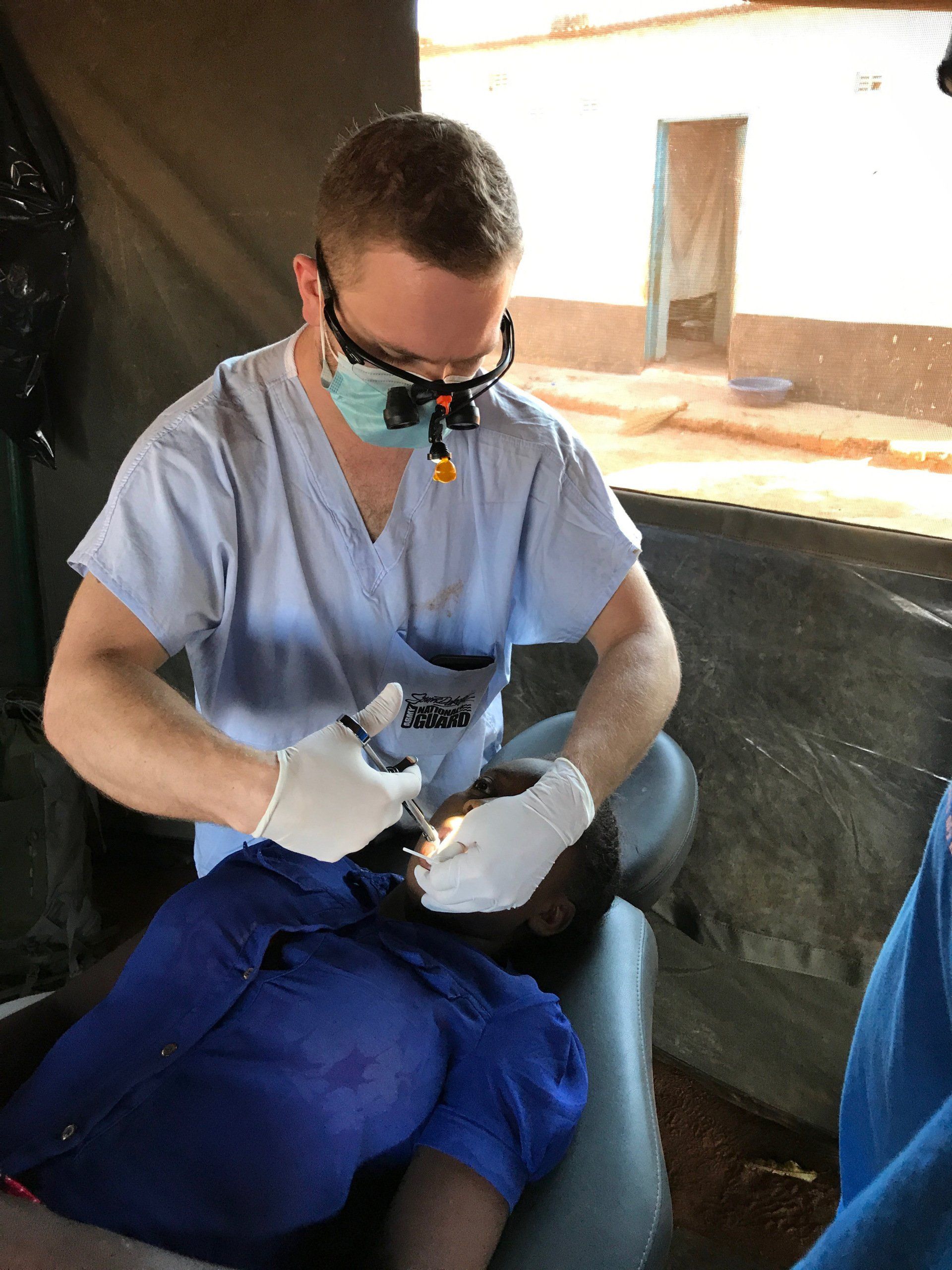A dentist is examining a child 's teeth in a tent.