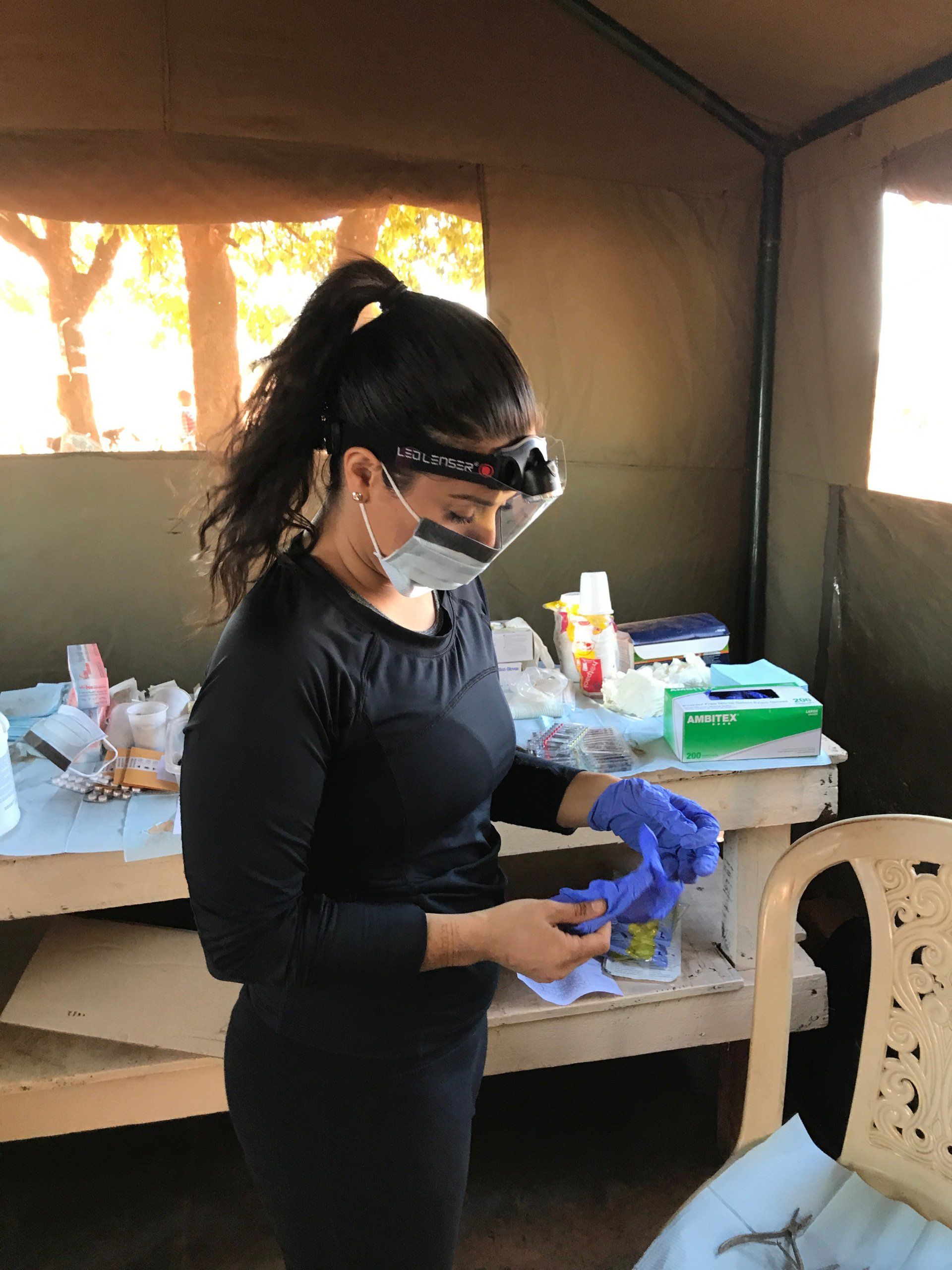 A woman wearing a mask and gloves is standing in a tent