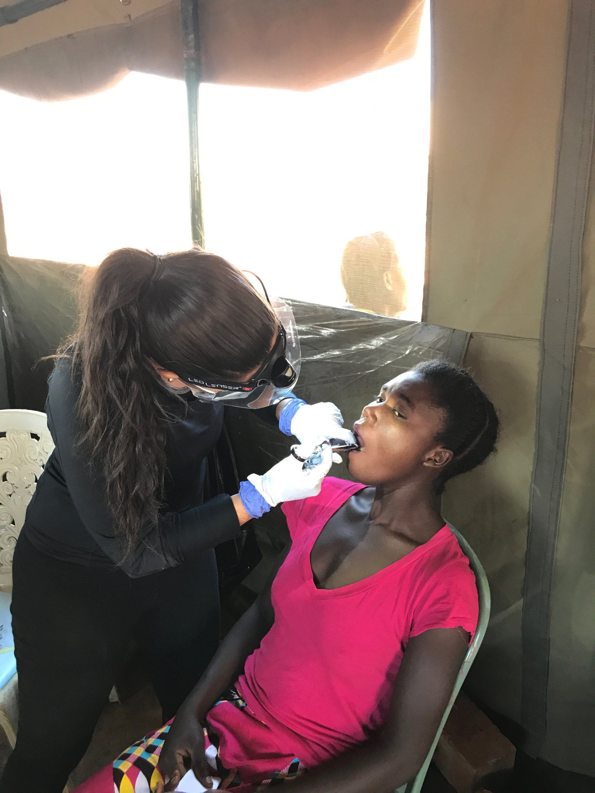 A woman in a pink shirt is getting her teeth examined by a dentist.