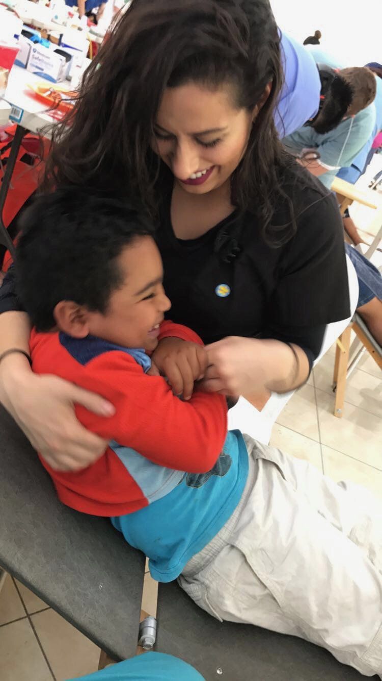 A woman is hugging a young boy who is laying on a table