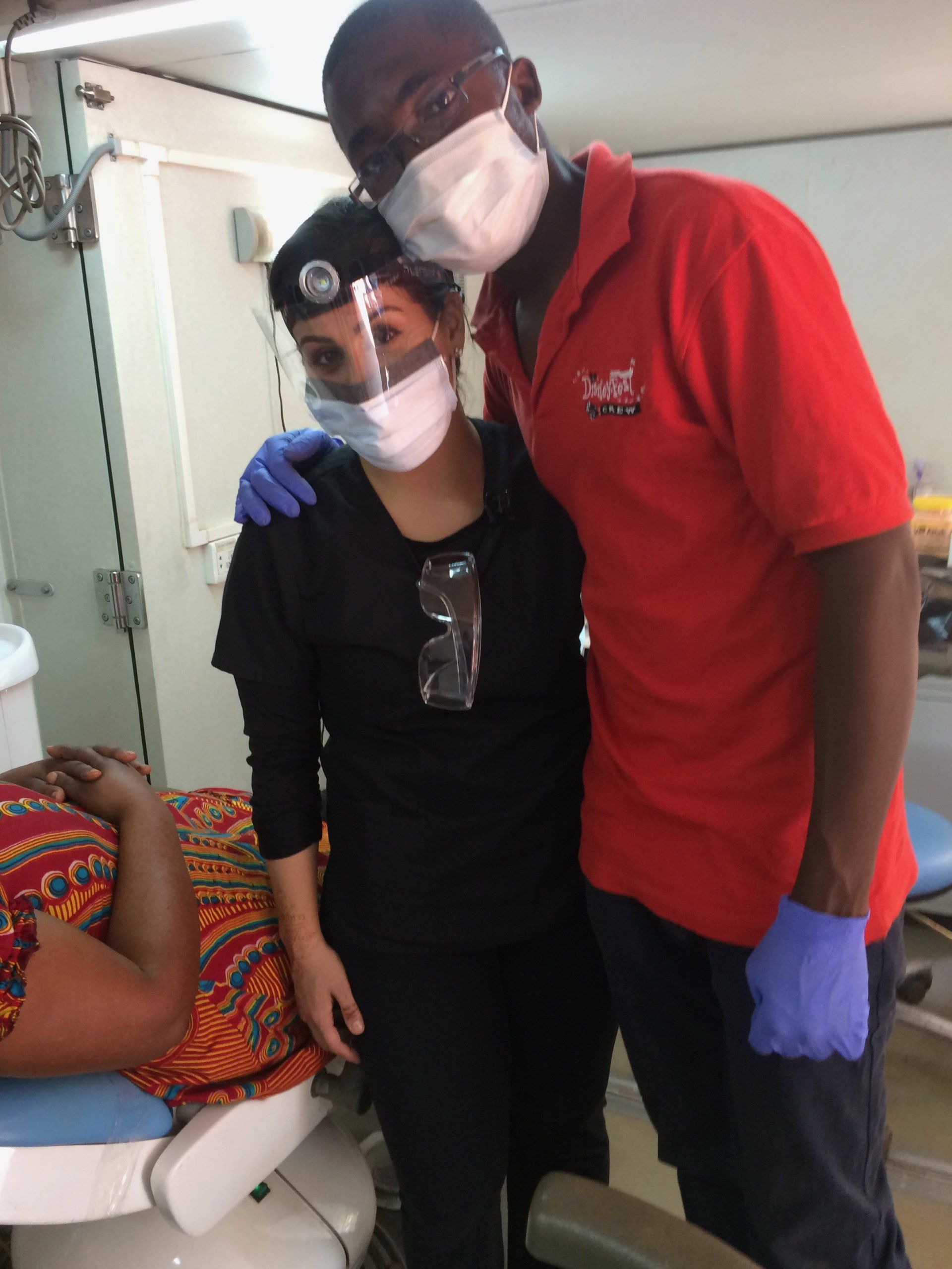 A man in a red shirt stands next to a woman wearing a mask