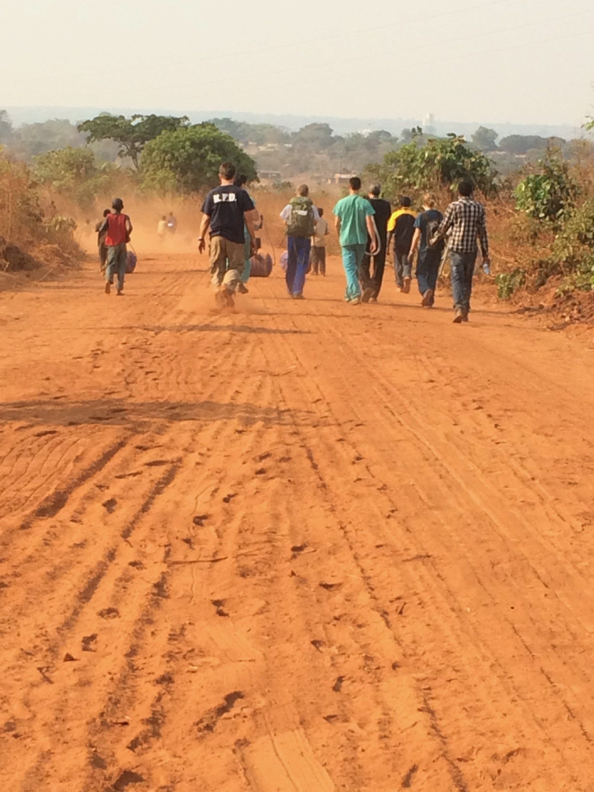 A group of people are walking down a dirt road